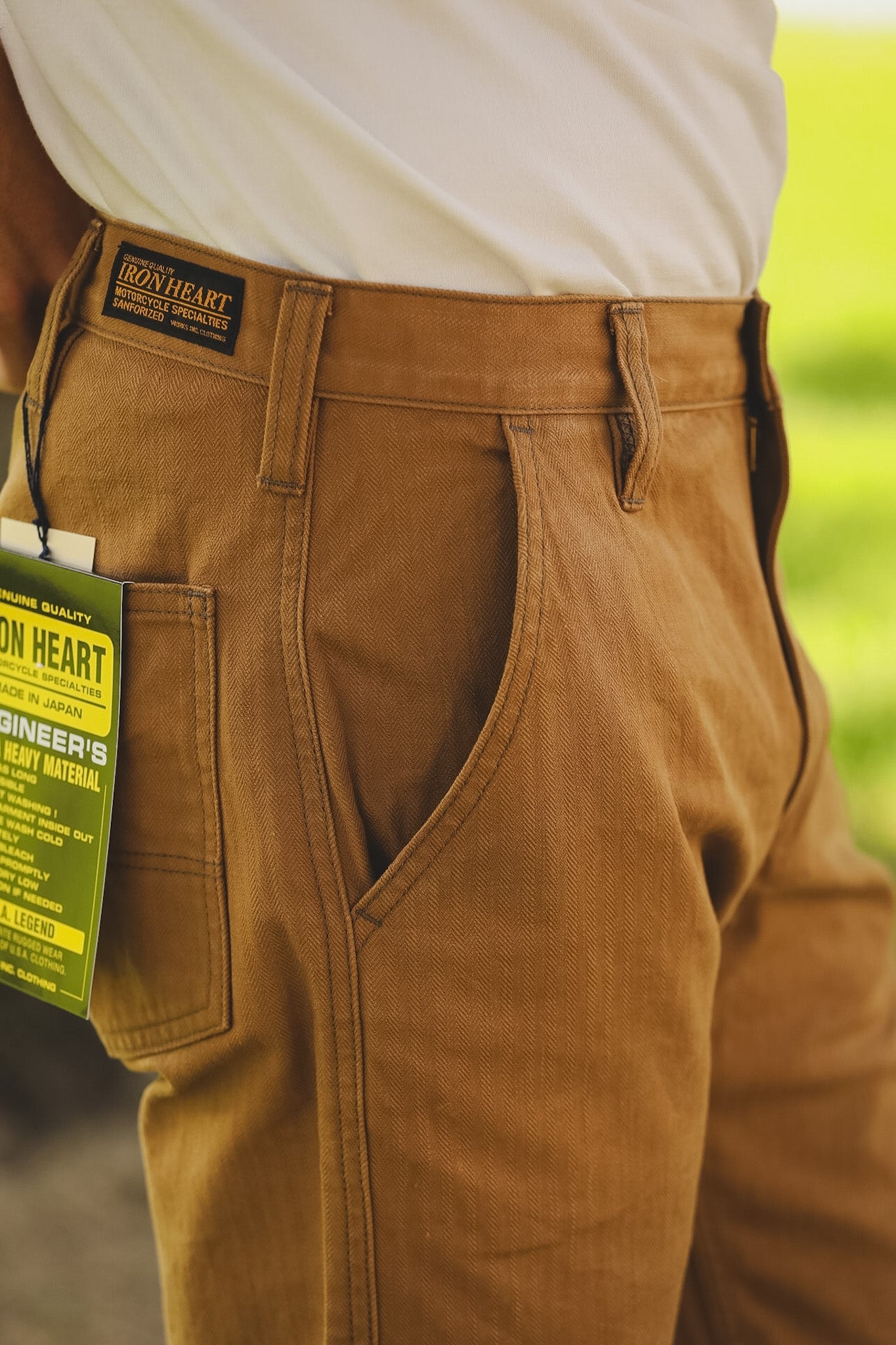 Brown pants with a visible brand tag against a blurred green background