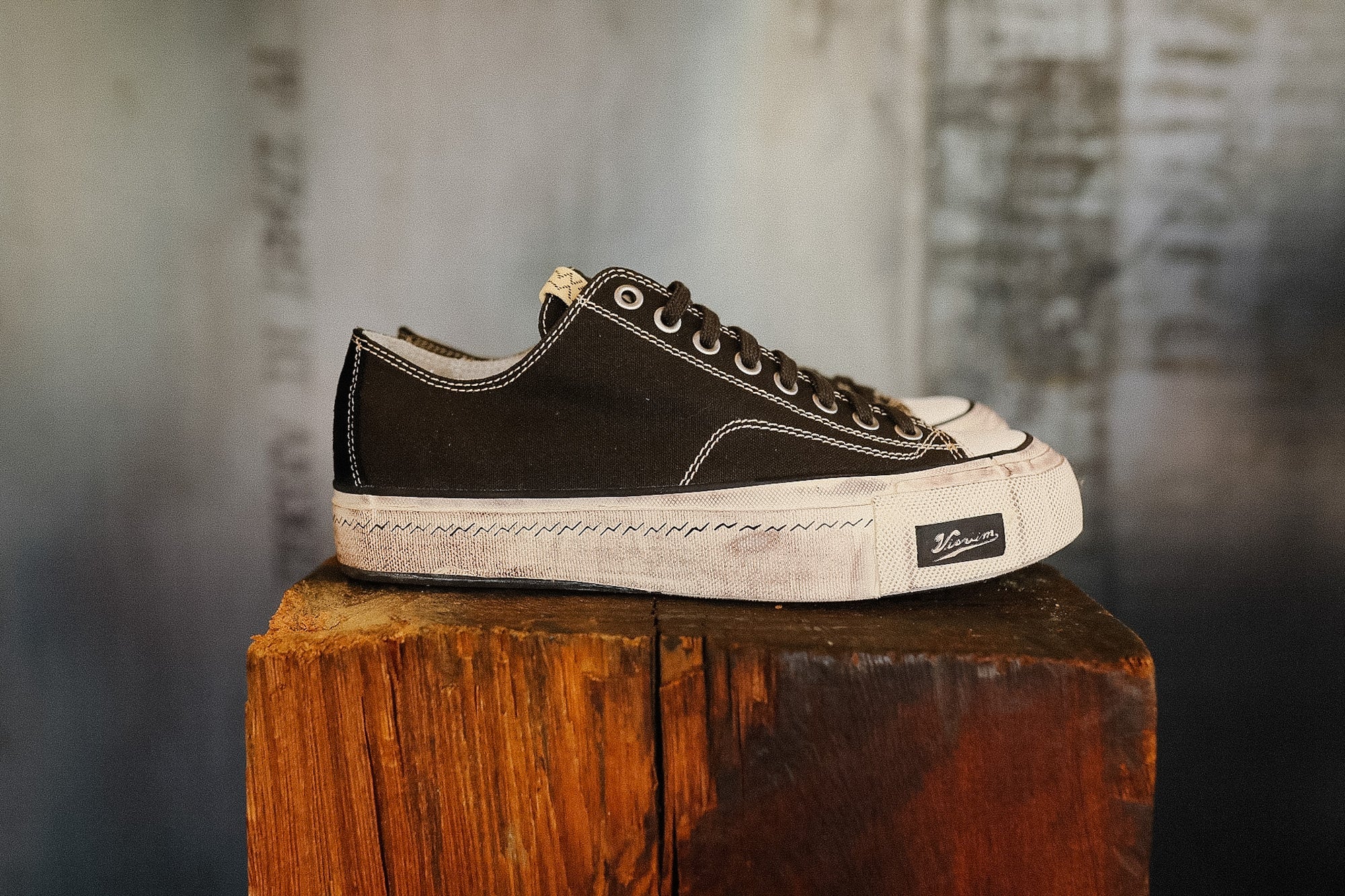 Black sneaker with white sole on a wooden block against a textured wall background