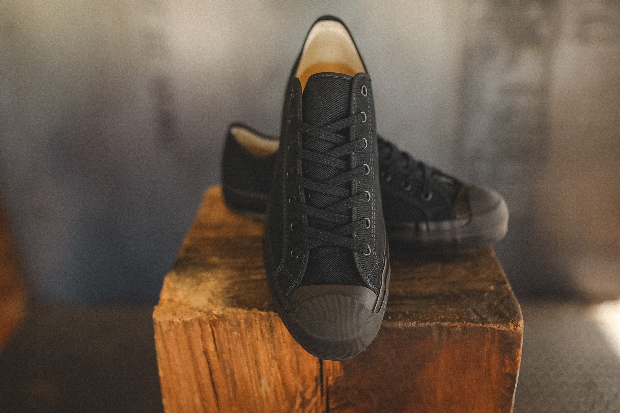 Up close image of a black sneaker on a wood block with a grey background 