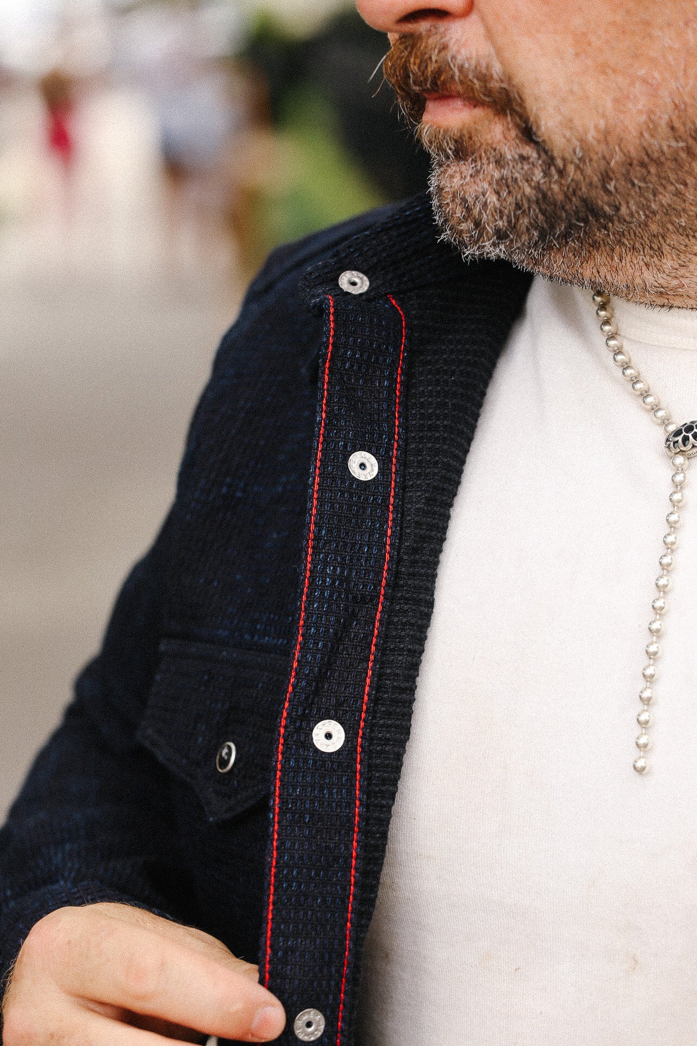 Close-up of a person wearing a dark jacket with red stitching and a white shirt.