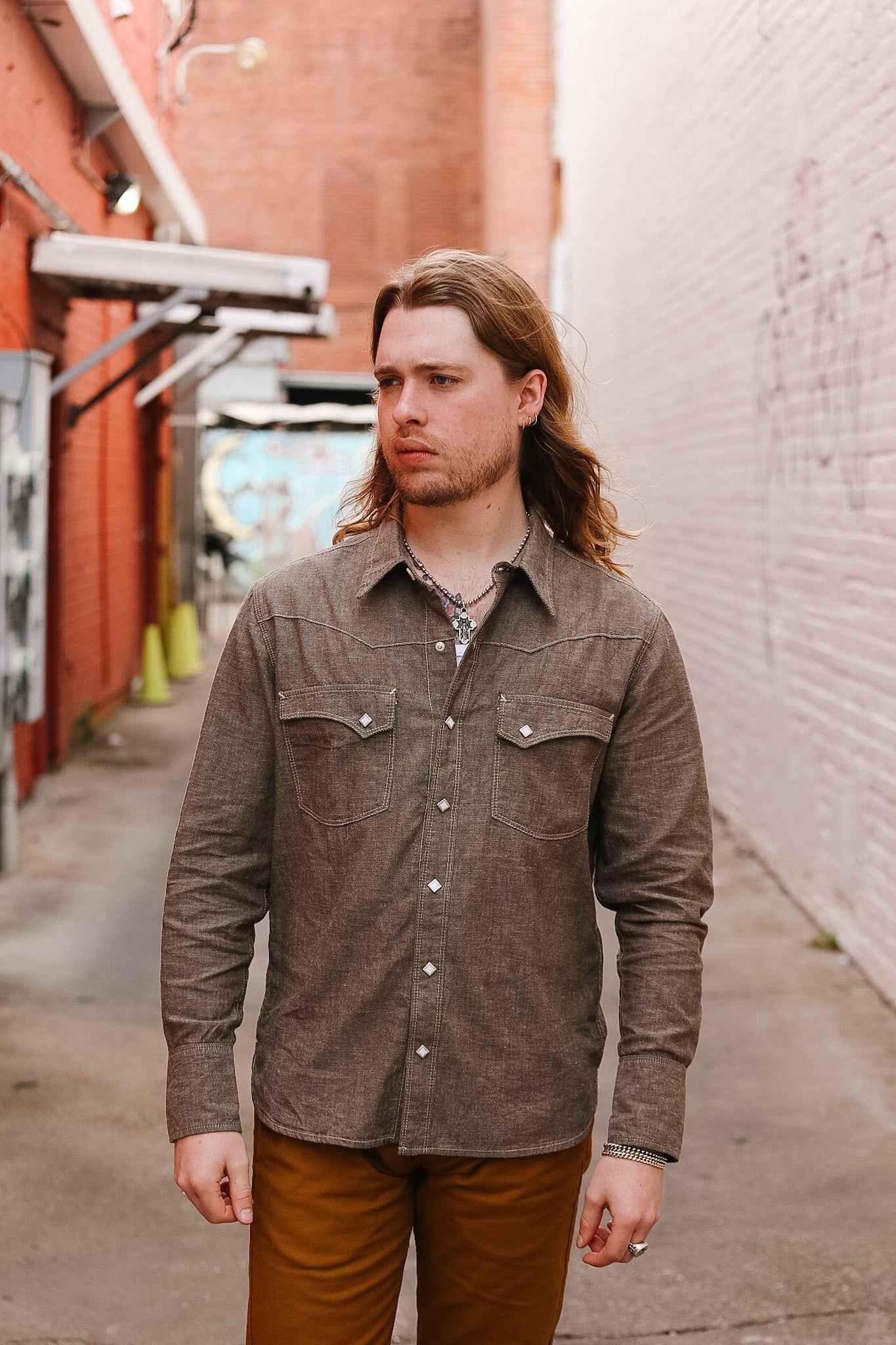 Man wearing a brown button-up shirt and brown pants walking down a street.