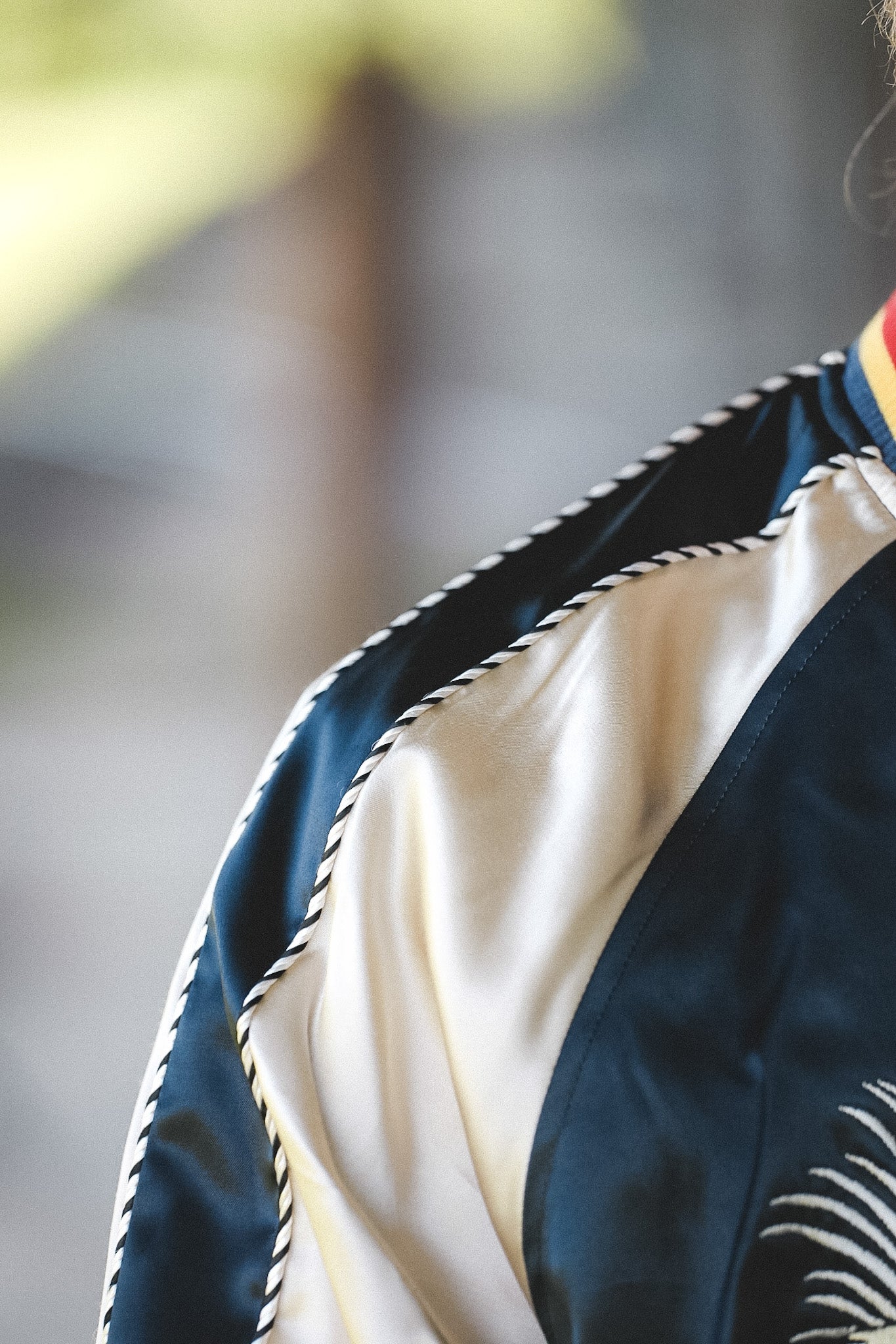 Close-up of a dark navy satin jacket with cream-colored lining and black-and-white rope trim along the shoulder seam.