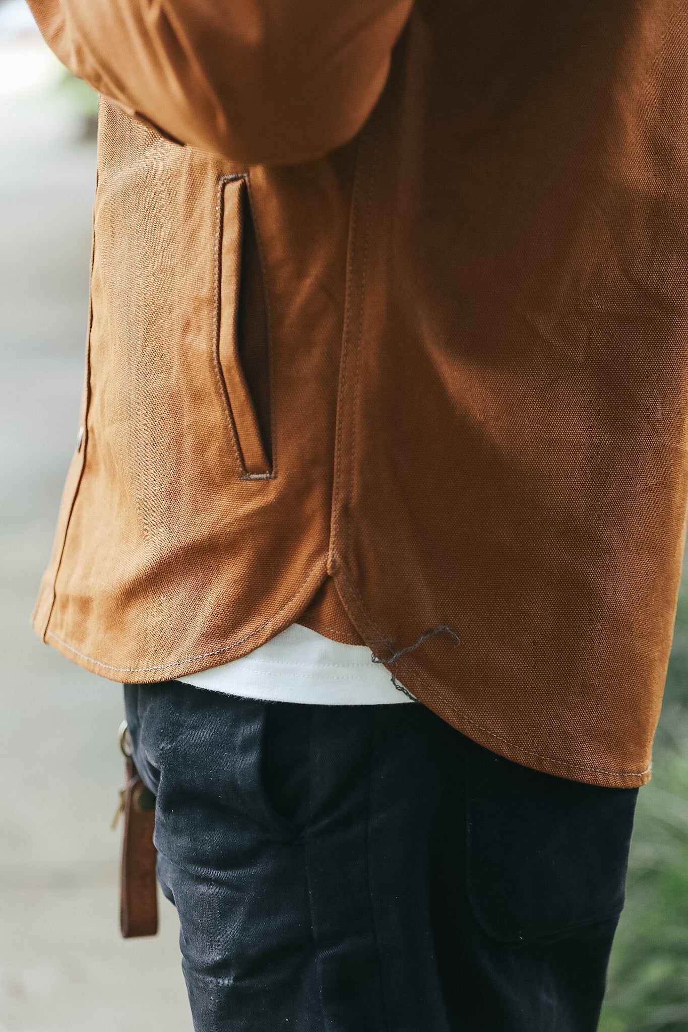 Close-up of a person wearing a rust-brown linen jacket with a vertical welt pocket, paired with dark blue jeans and a white undershirt.