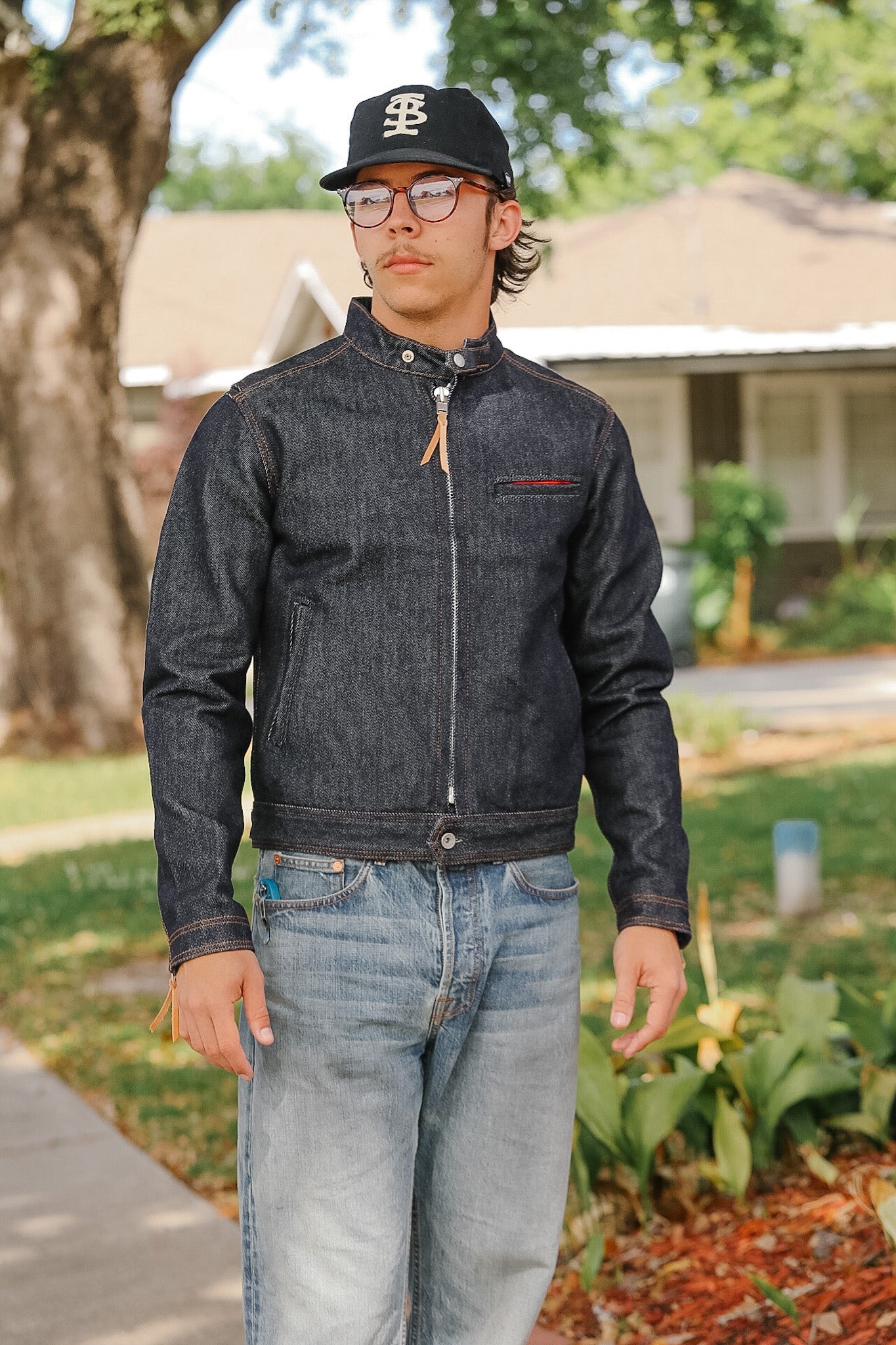 Person wearing a dark denim jacket and jeans standing outdoors.
