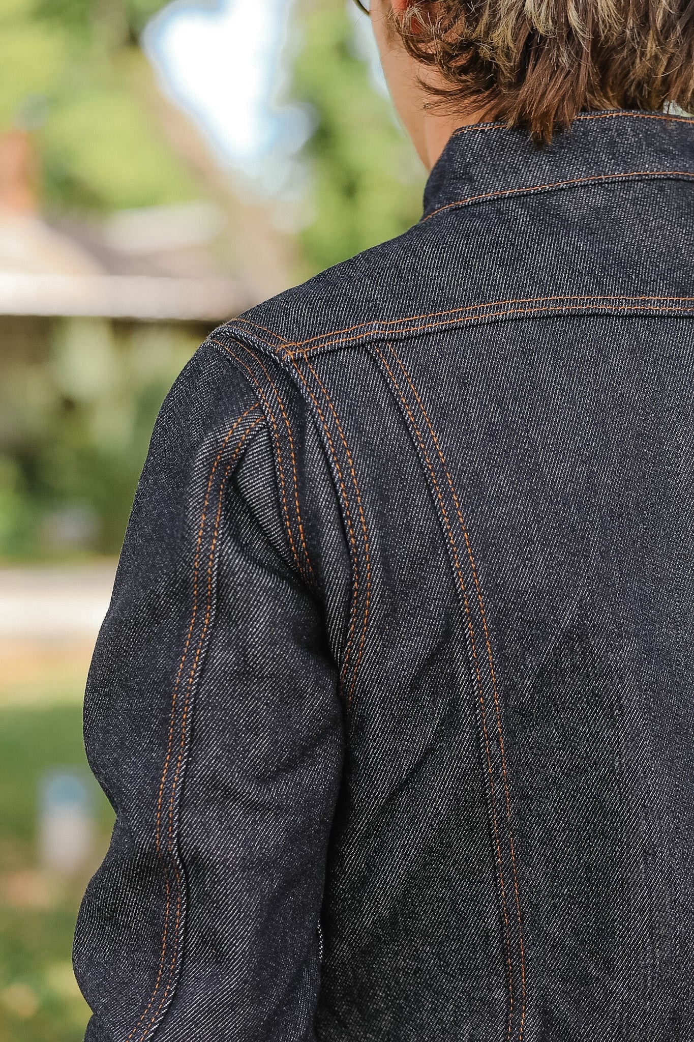 Close-up of a person wearing a dark denim jacket with a blurred outdoor background