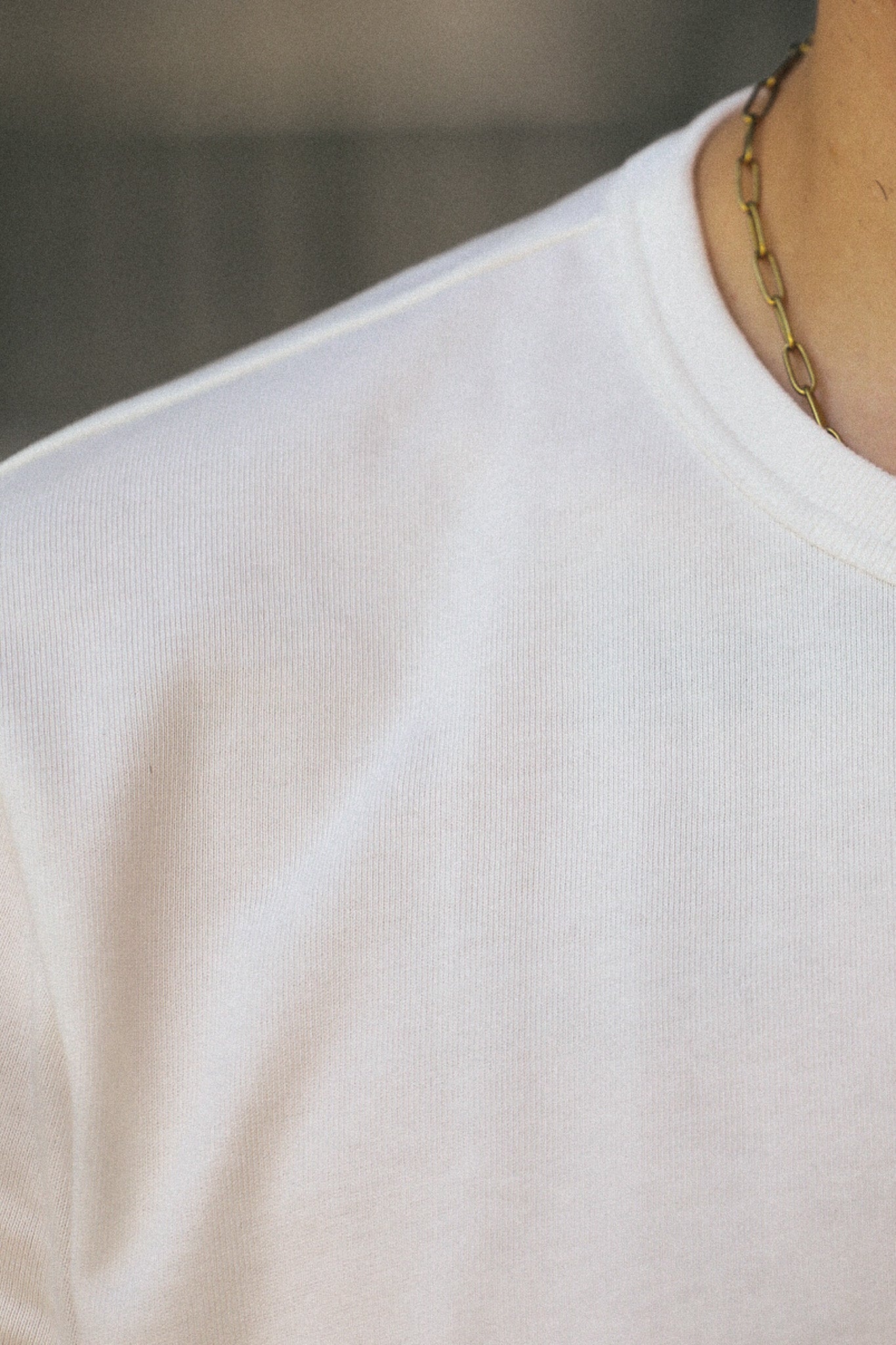 Close-up of a person wearing a plain white crew-neck t-shirt and a gold chain necklace, with the focus on the shirt's texture and neckline.