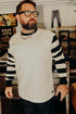 Bearded man wearing black and white striped long sleeve shirt and glasses in vintage-style clothing store