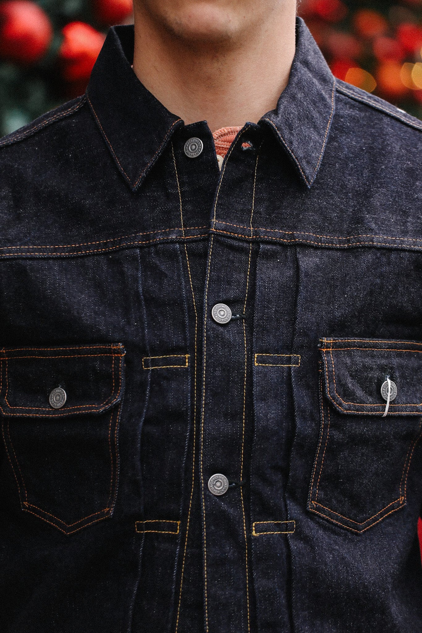 Close-up of a person wearing a dark denim jacket with orange stitching and metal buttons