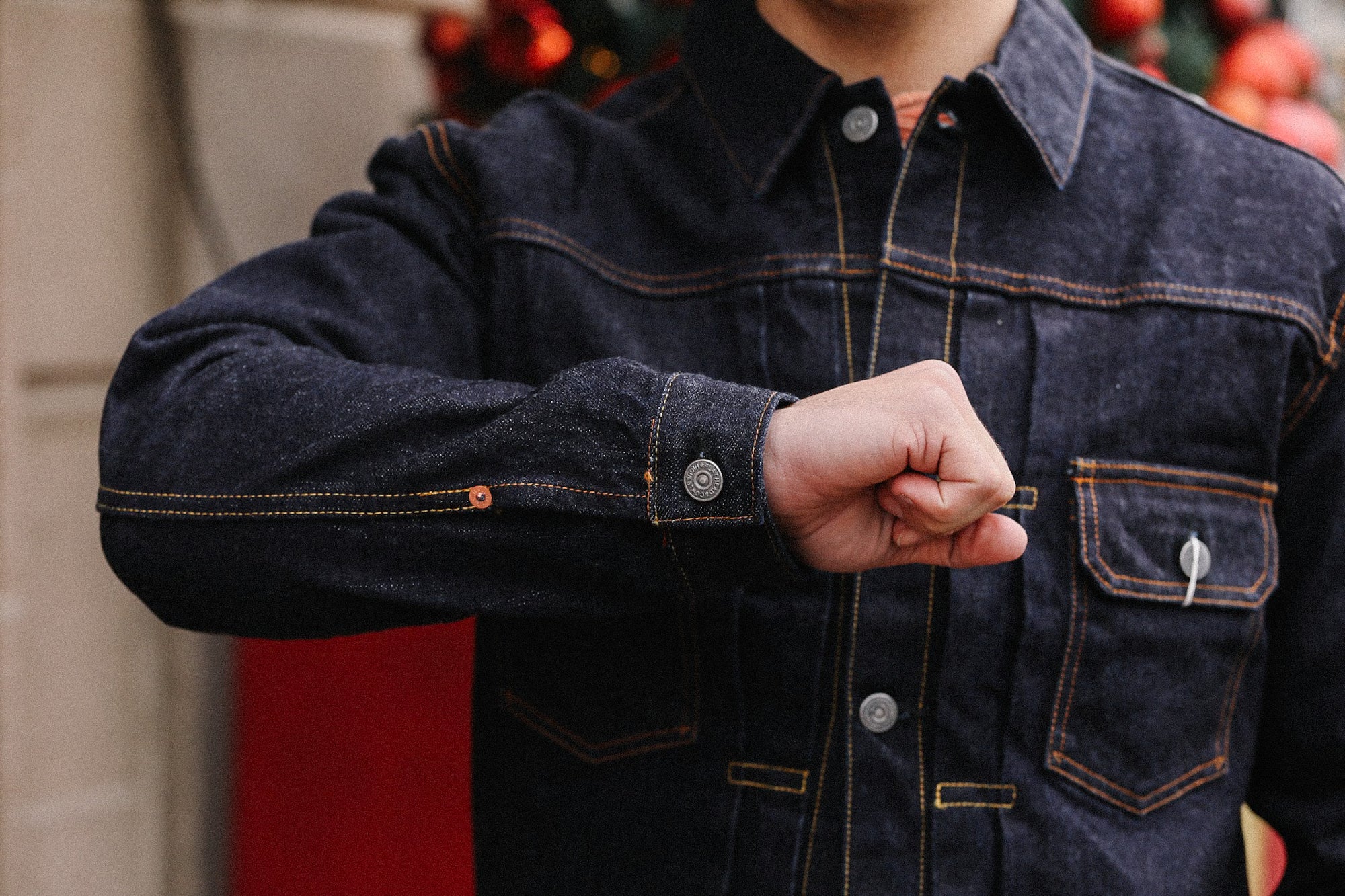 Close-up of a person wearing a dark denim jacket with orange stitching and metal buttons, fist raised
