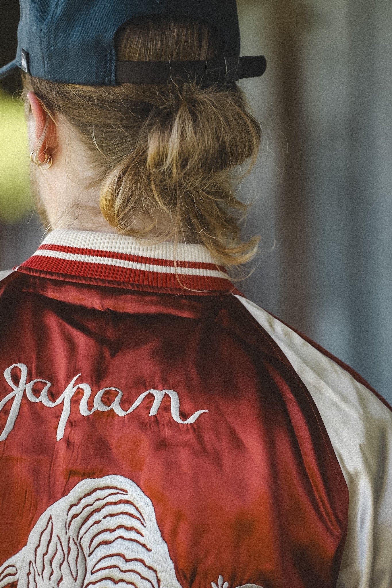 Close-up of the back of a satin bomber jacket in deep red, featuring a large white embroidered tiger, bamboo, and the word 'Japan' in white script.