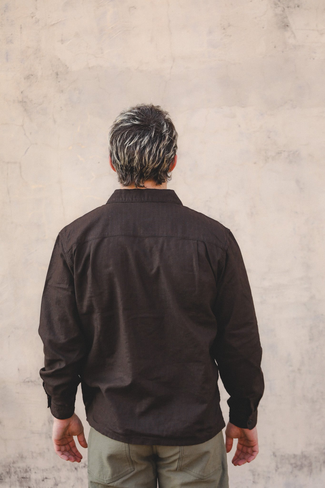 Man wearing a dark brown shirt against a textured beige wall