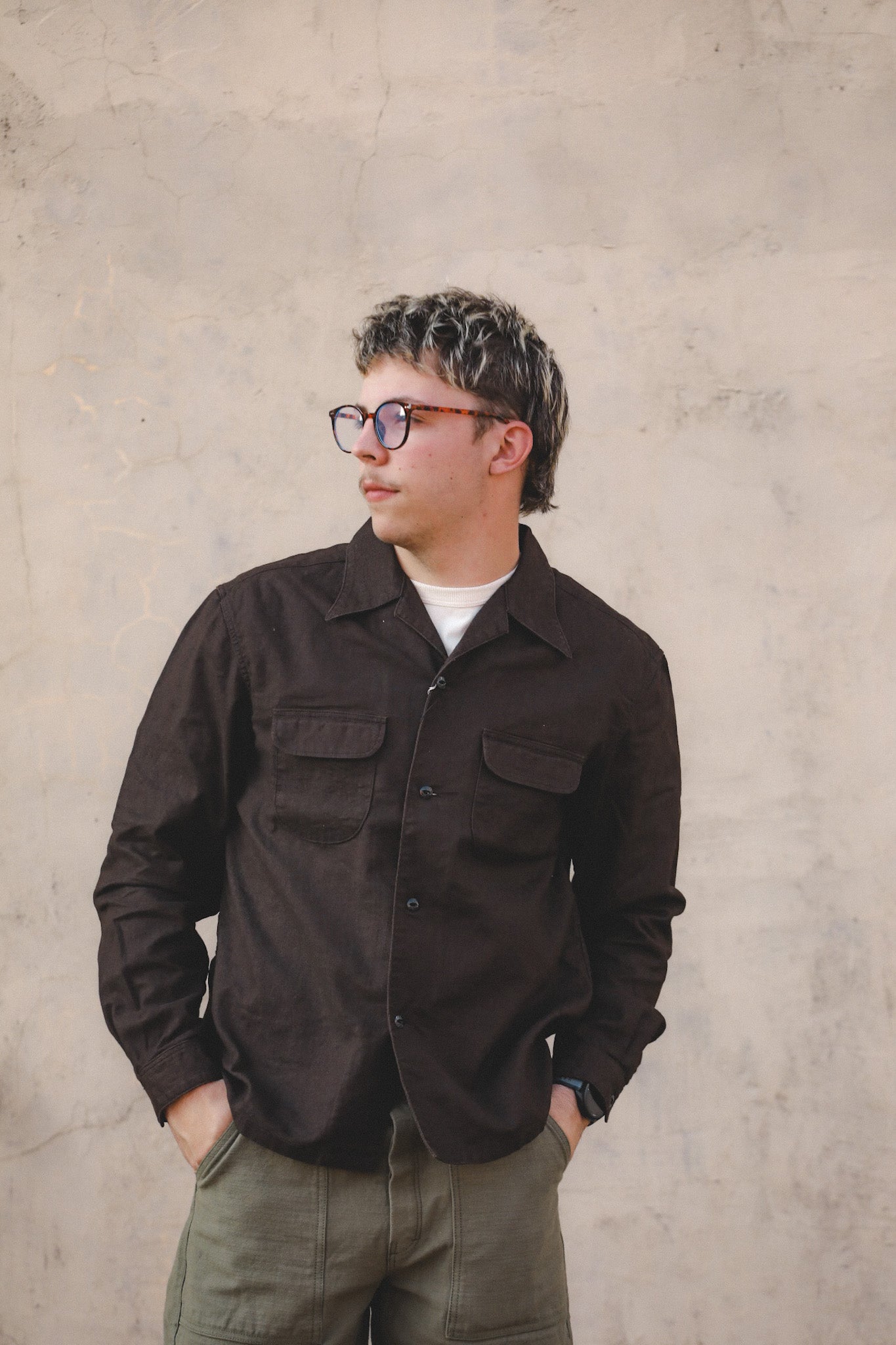 Person wearing a dark brown jacket and glasses against a plain background