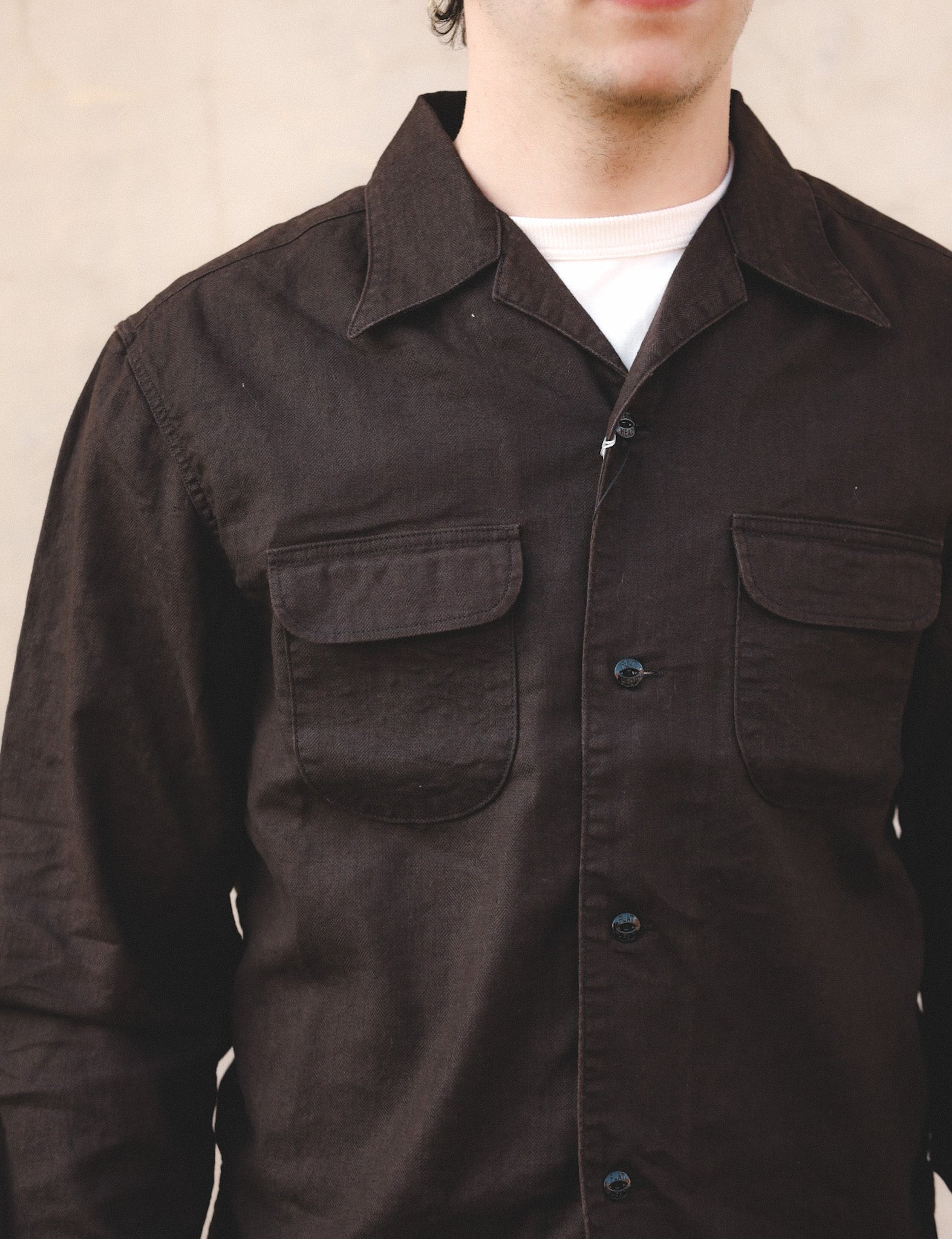 Close-up of a person wearing a dark brown shirt with a plain background