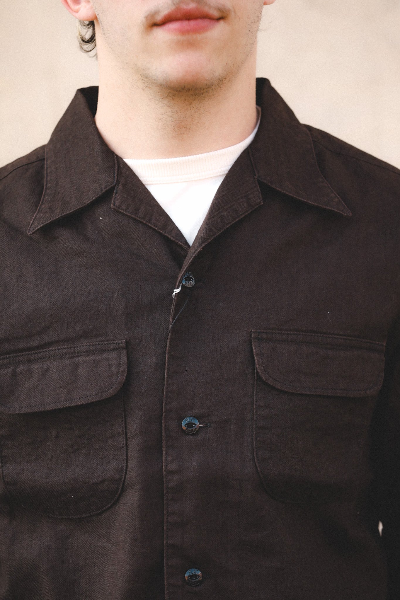 Close-up of a person wearing a dark brown jacket with a plain background