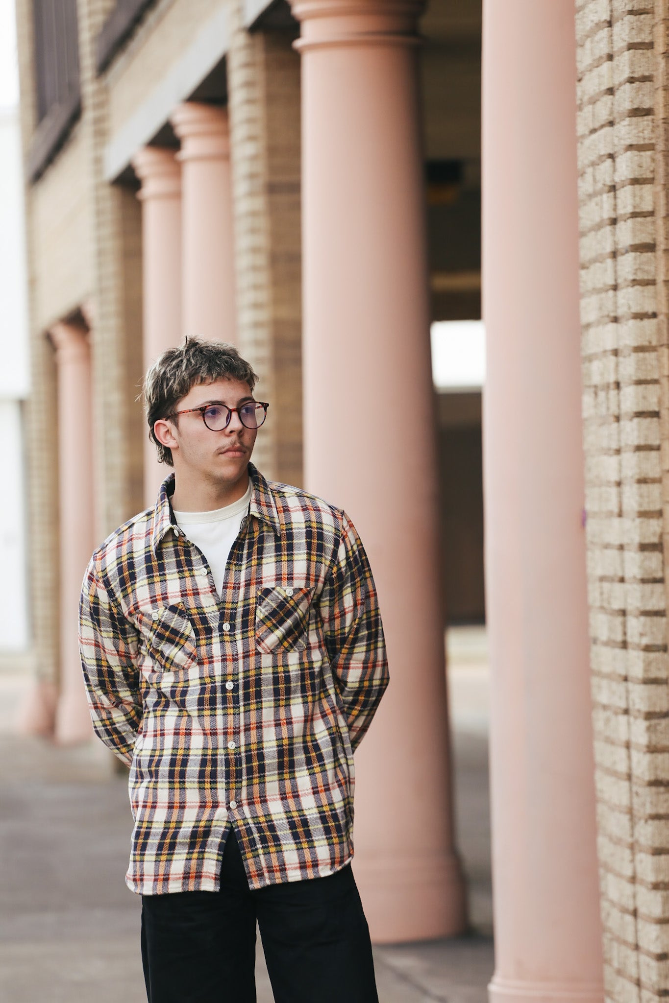 Person wearing a plaid shirt standing in front of a building with columns