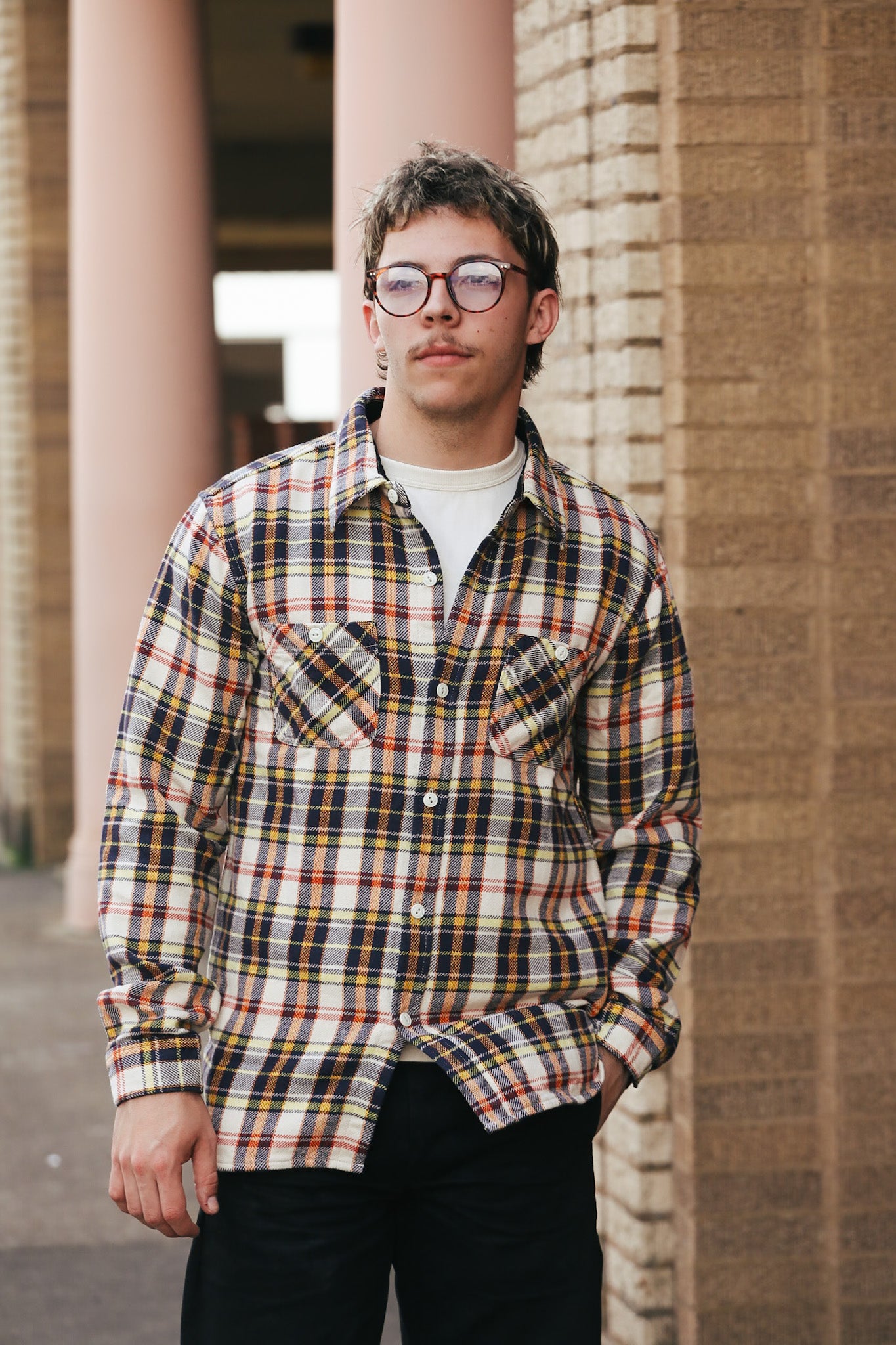 Person wearing a plaid shirt standing against a brick wall.