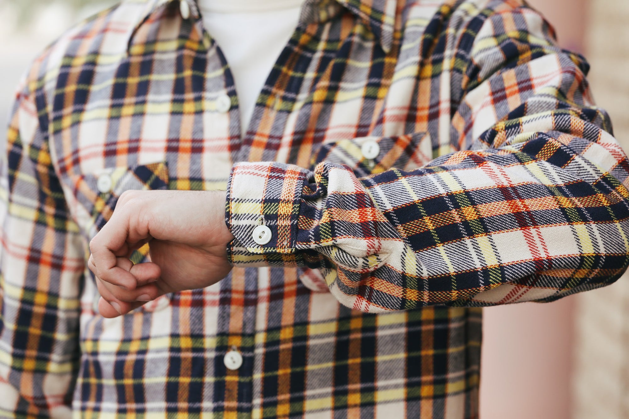 Close-up of a person wearing a plaid shirt with rolled-up sleeves.