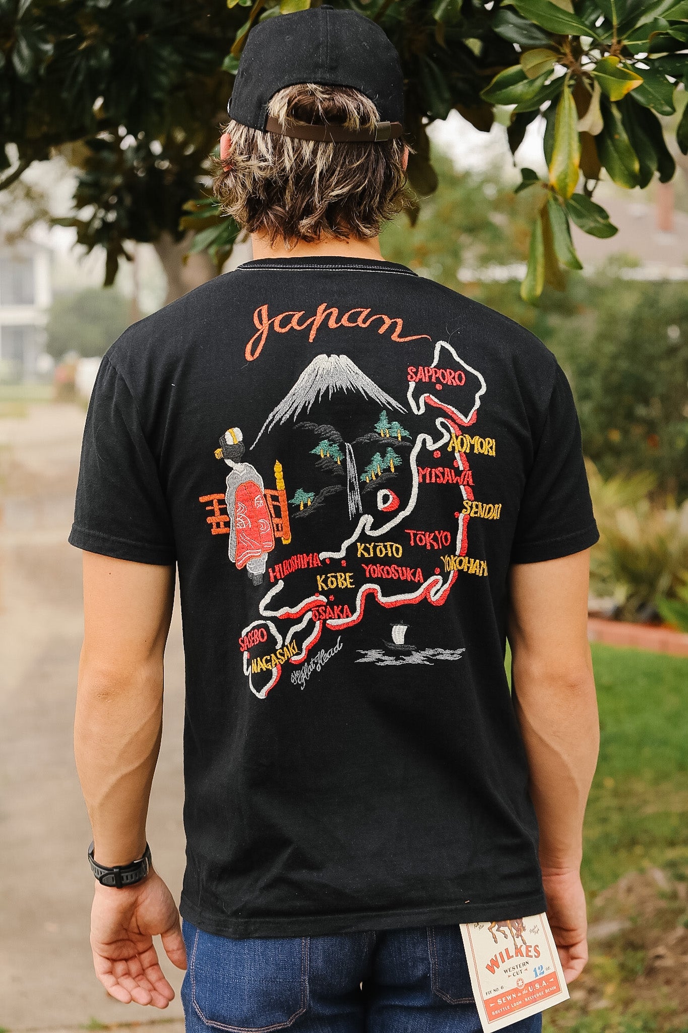 Person wearing a black t-shirt with colorful graphics and text, standing outdoors.