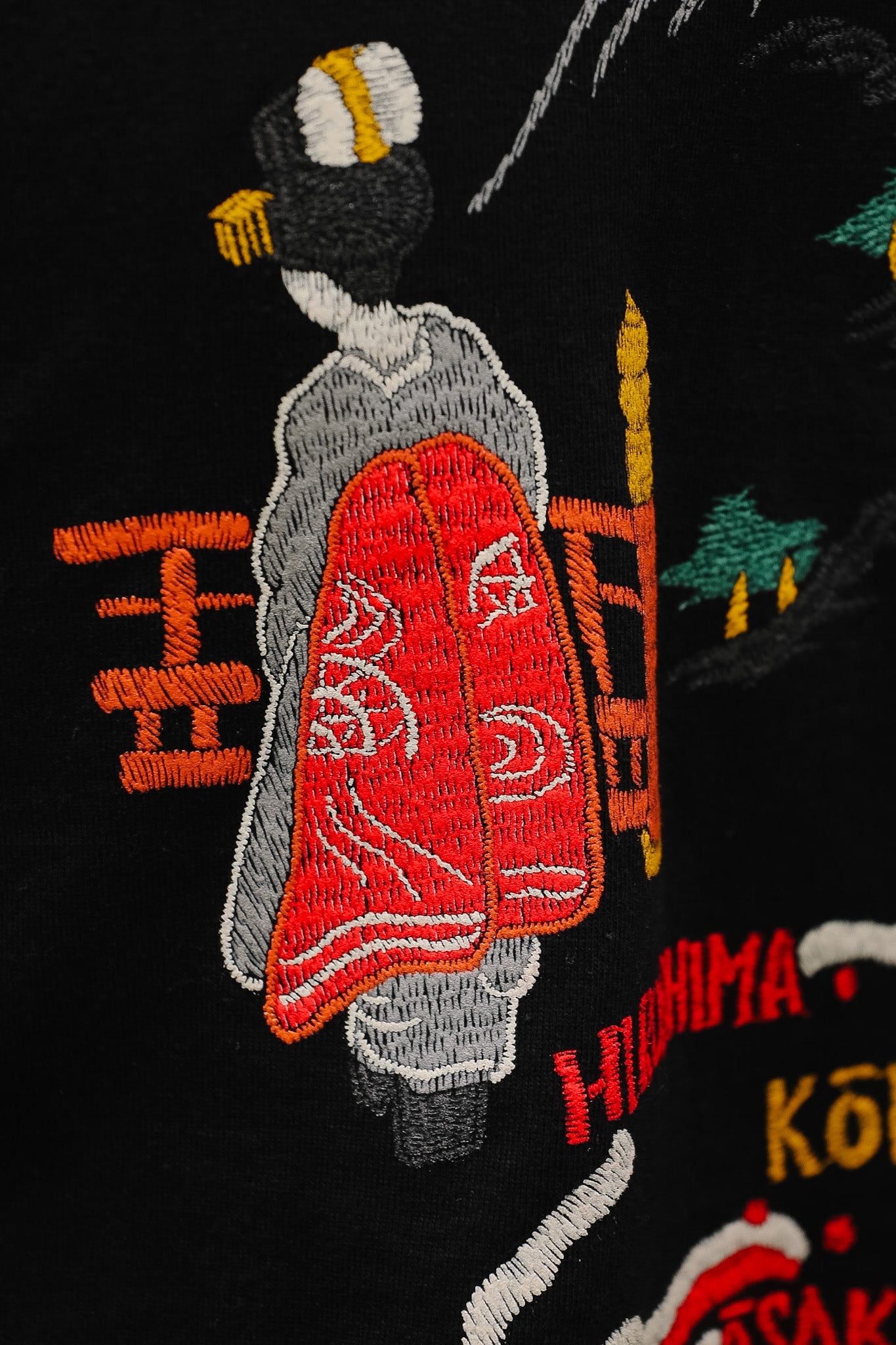 Embroidered design of a person in traditional attire with a red cape on a black background.