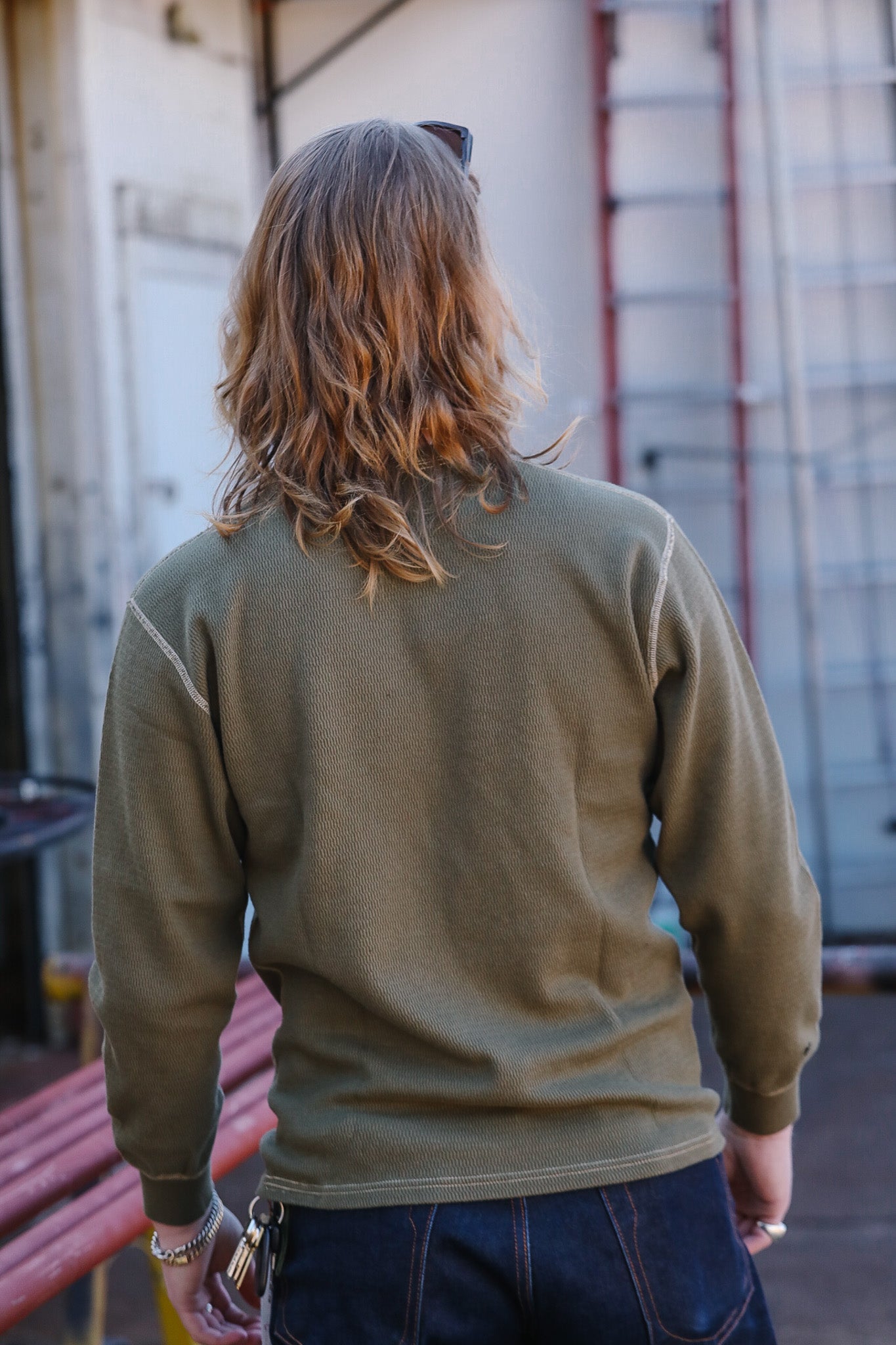 Person wearing a green sweatshirt with long hair, standing in an industrial setting.