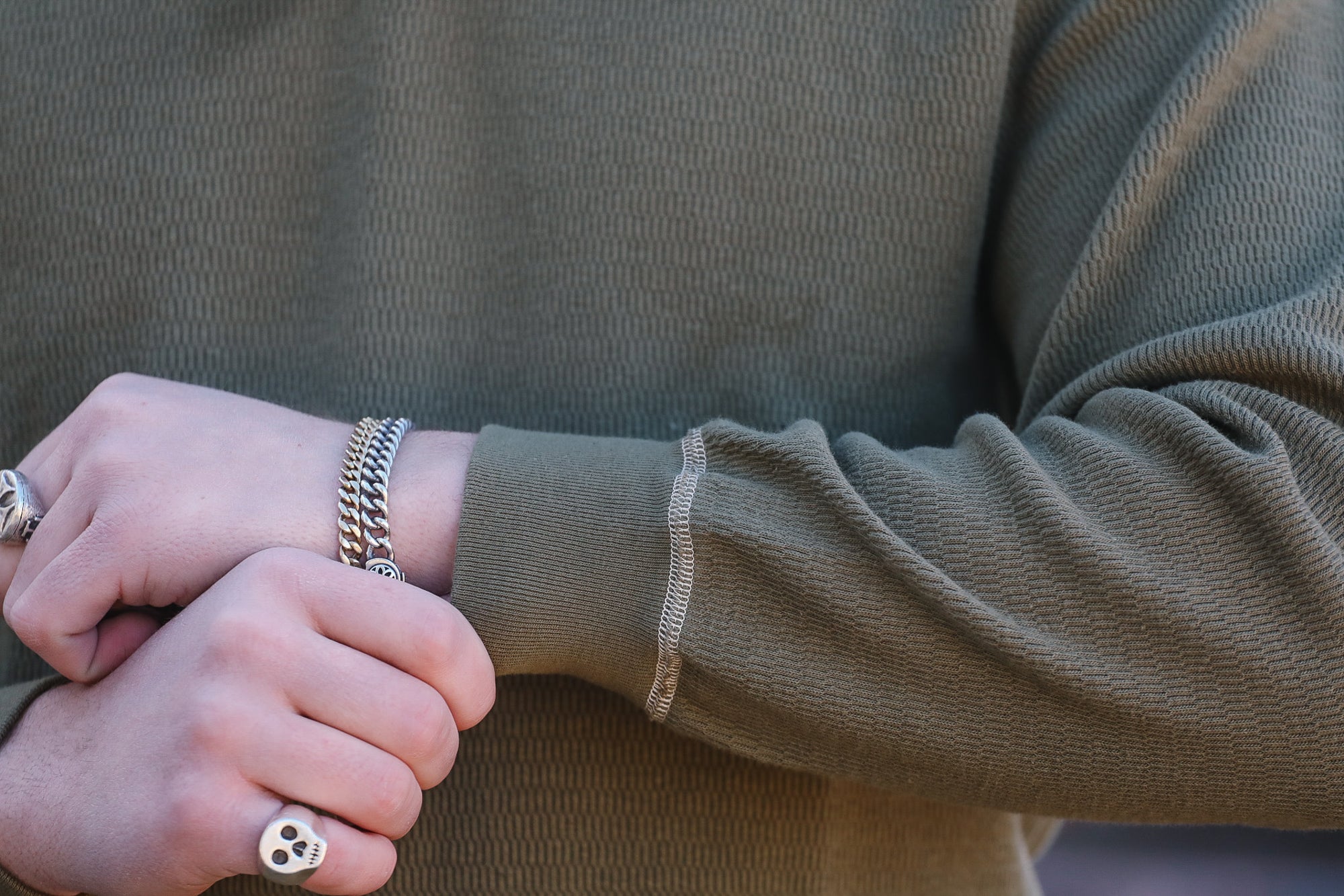 Close-up of a person wearing a green sweater with a bracelet and ring.