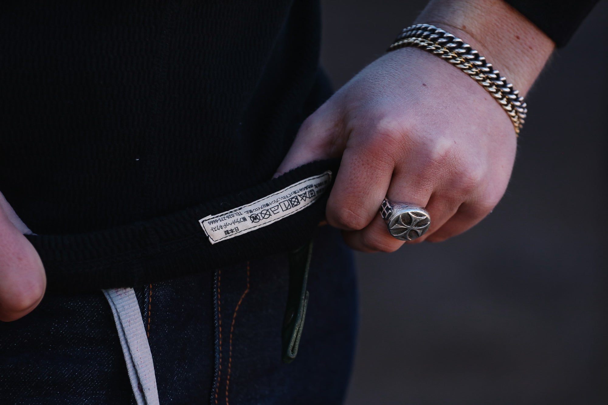 Person adjusting a belt with a visible brand label, wearing a gold bracelet and ring.