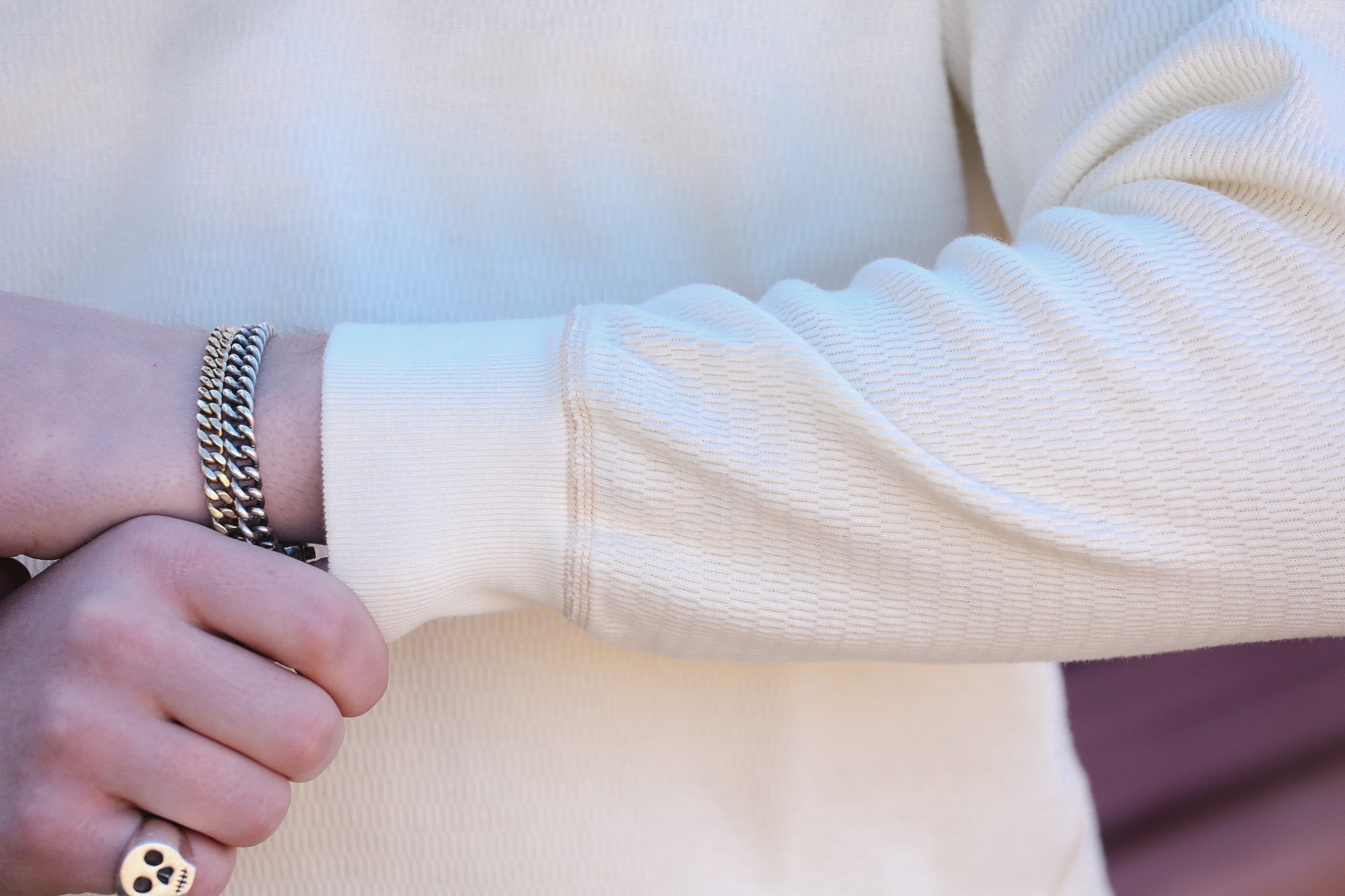 Close-up of a person wearing gold bracelets and a ring on a light background