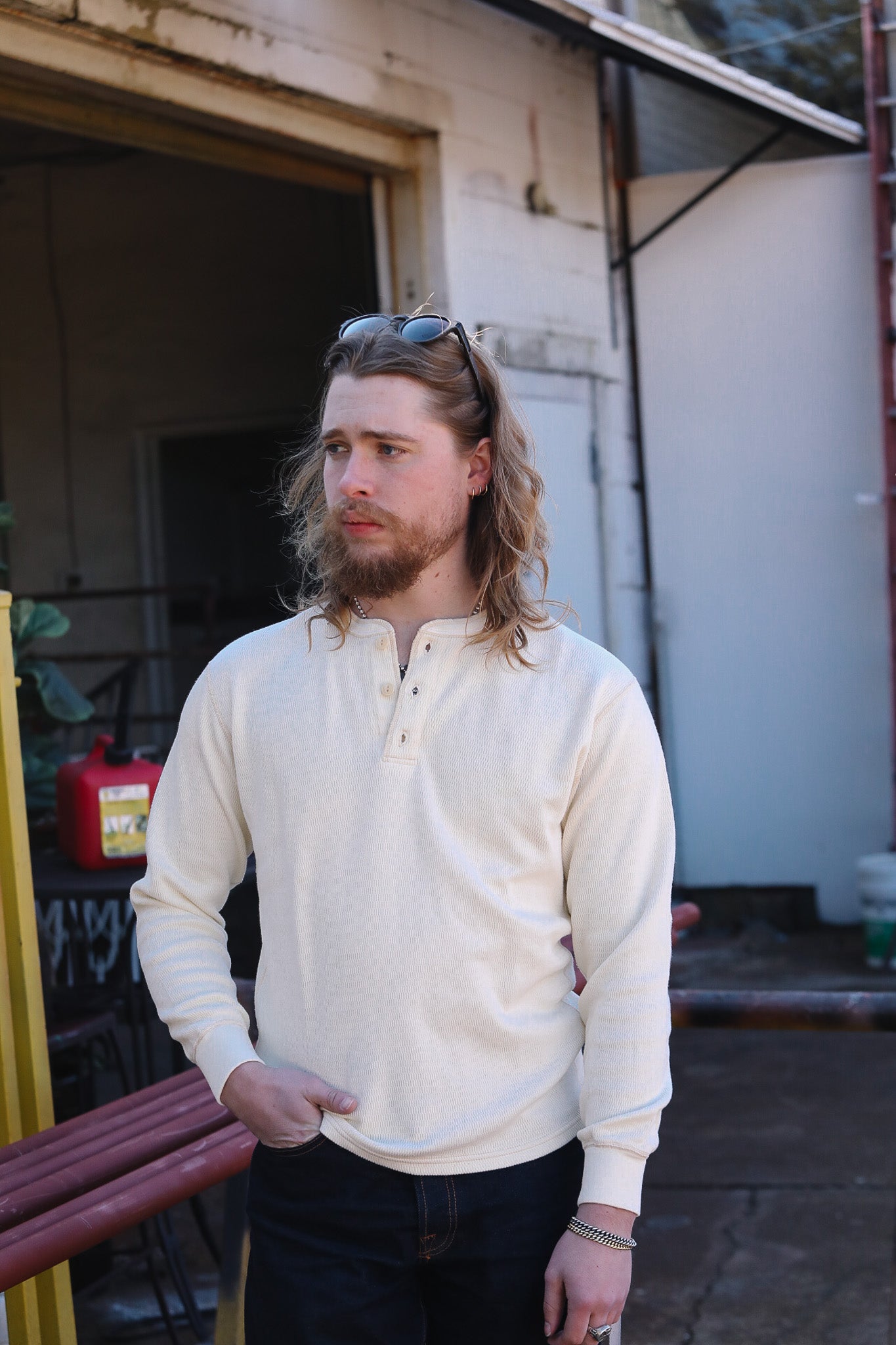 Man with long hair and beard wearing a white shirt standing outdoors.