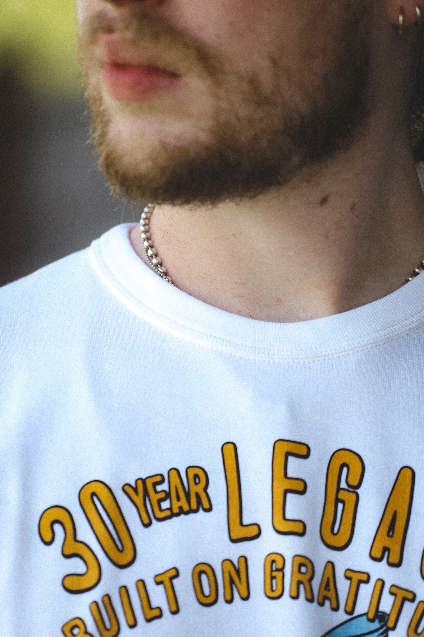 Close-up of a man wearing a white graphic t-shirt with yellow text that reads '30 YEAR LEGAL BUILT ON GRATITUDE'.