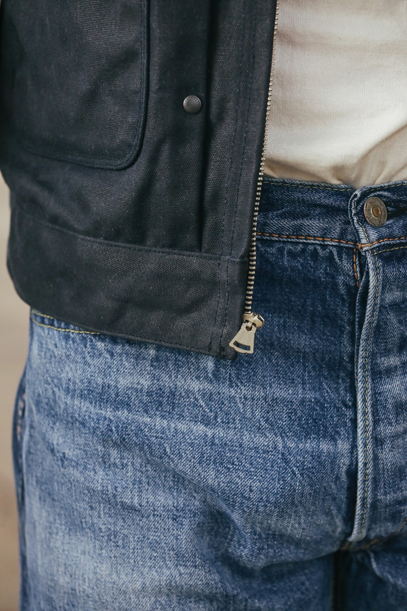 Close-up of a person wearing a dark jacket and blue jeans with a blurred background