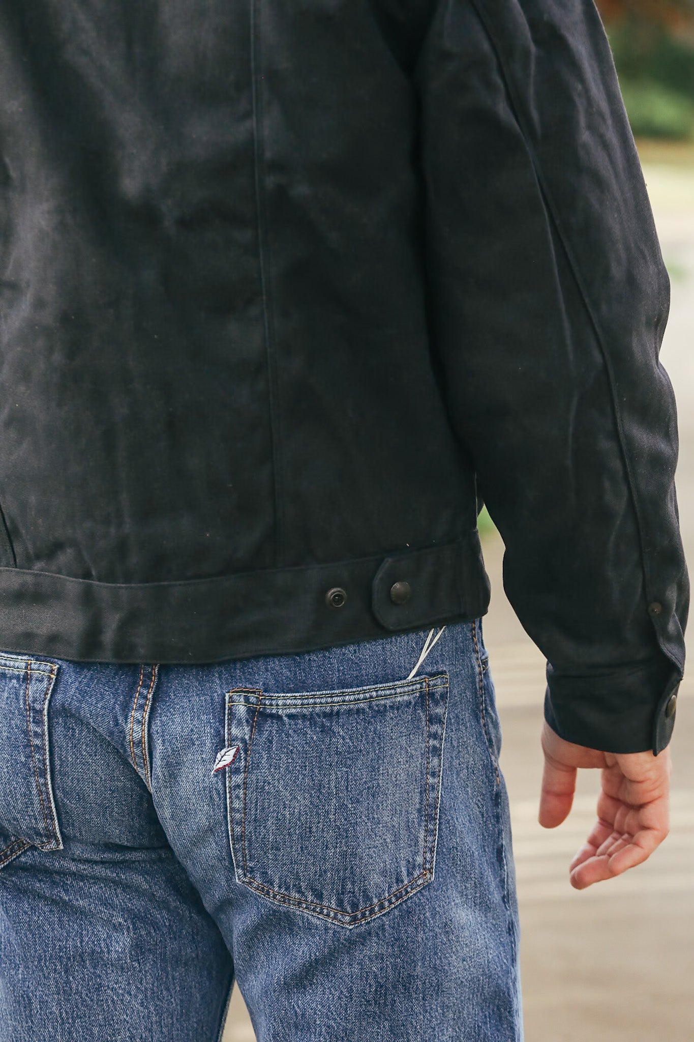 Person wearing a black jacket and blue jeans with a blurred background