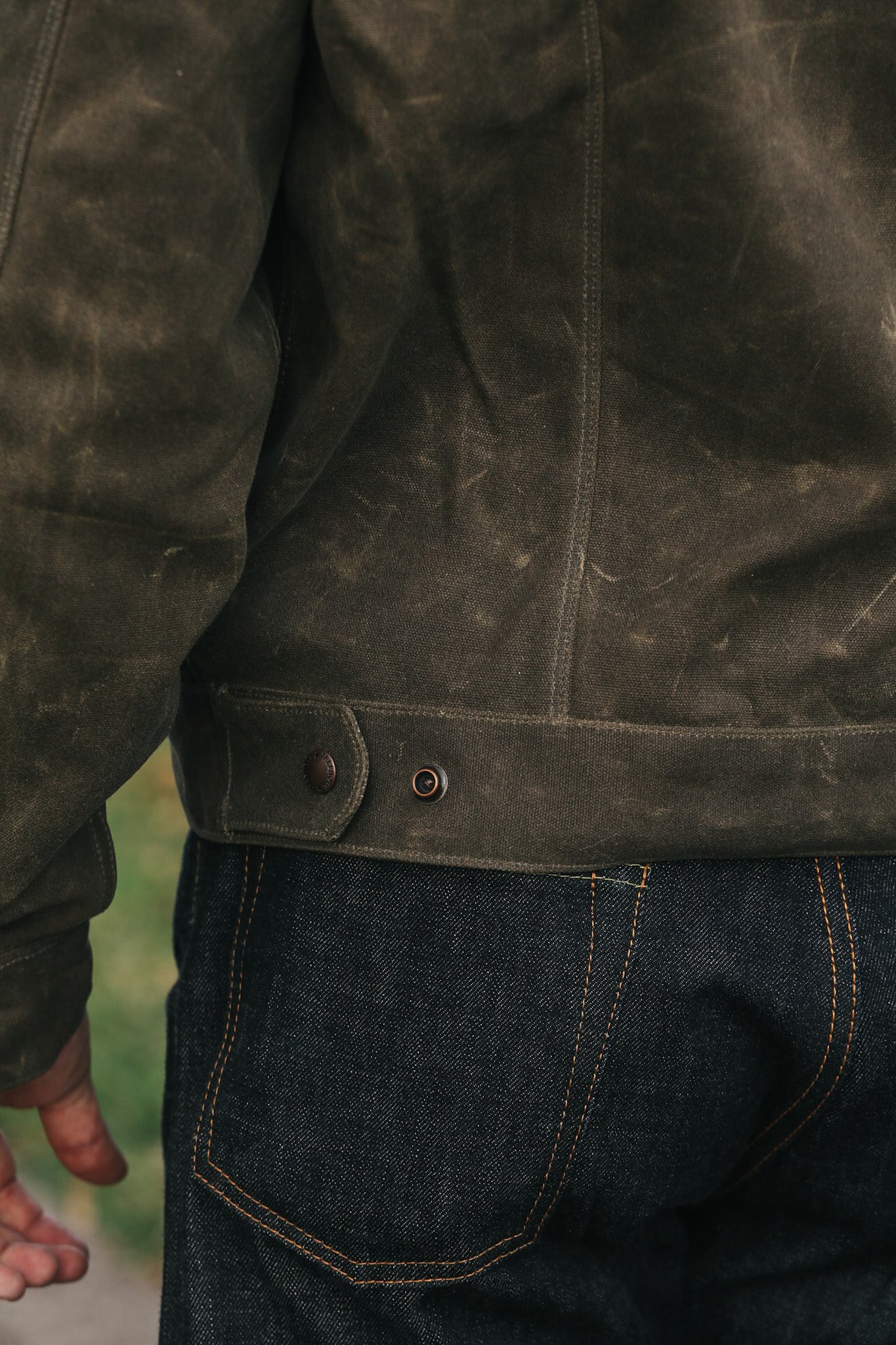 Close-up of a dark brown leather jacket and blue jeans with a blurred background
