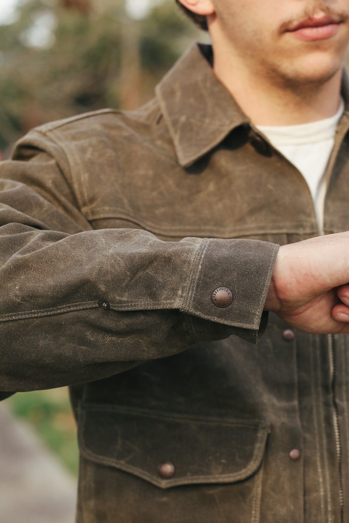 Close-up of a person wearing a brown leather jacket with a blurred natural background