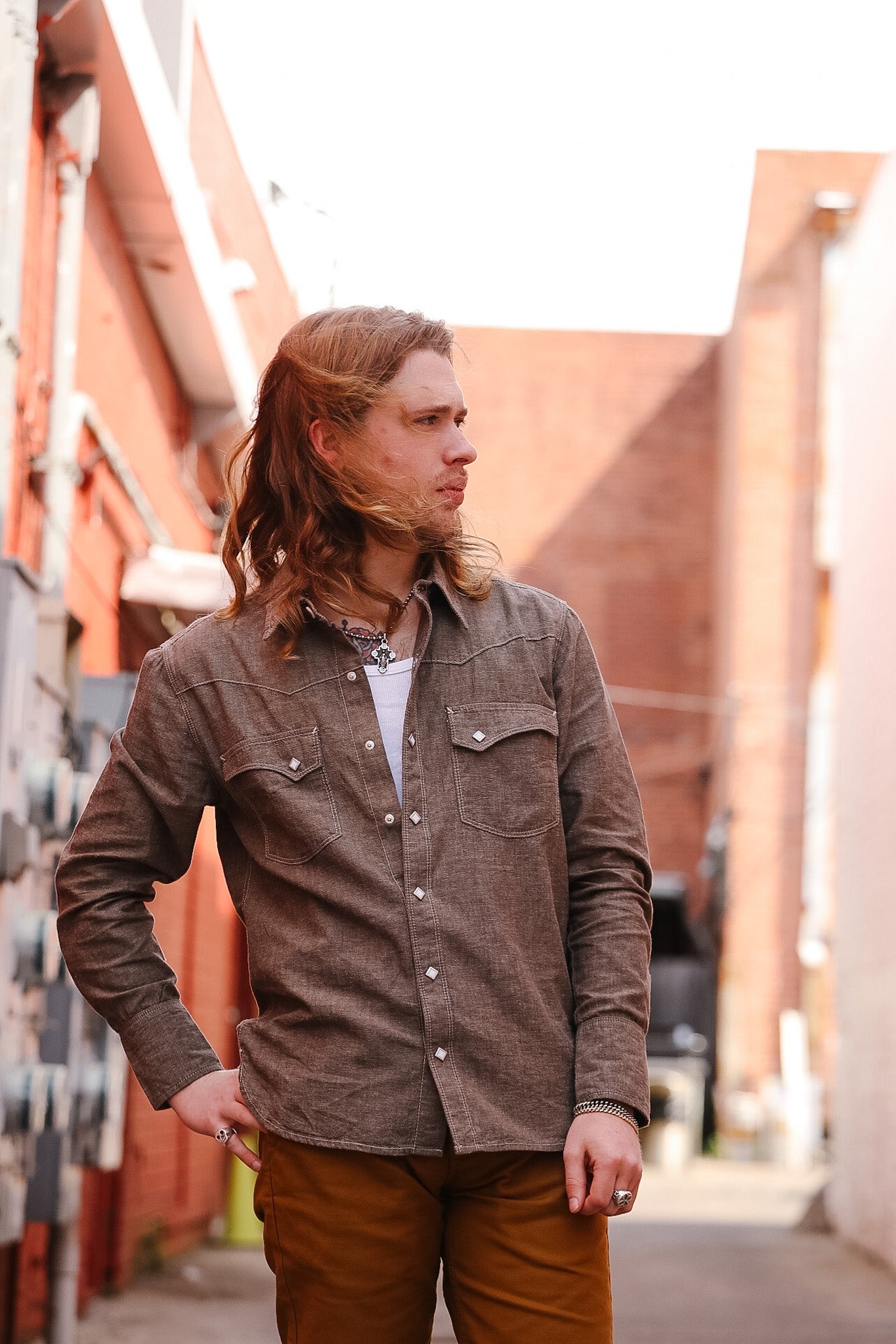 Man wearing a brown shirt and pants standing in an alleyway.