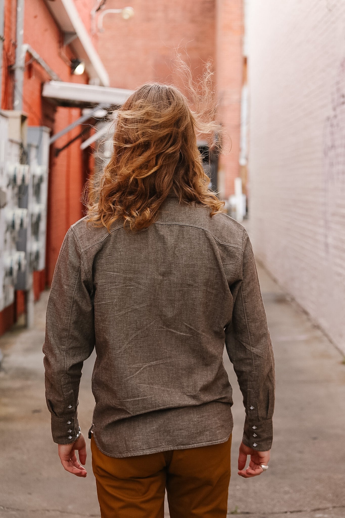 Person wearing a brown jacket and pants walking away in an alleyway.