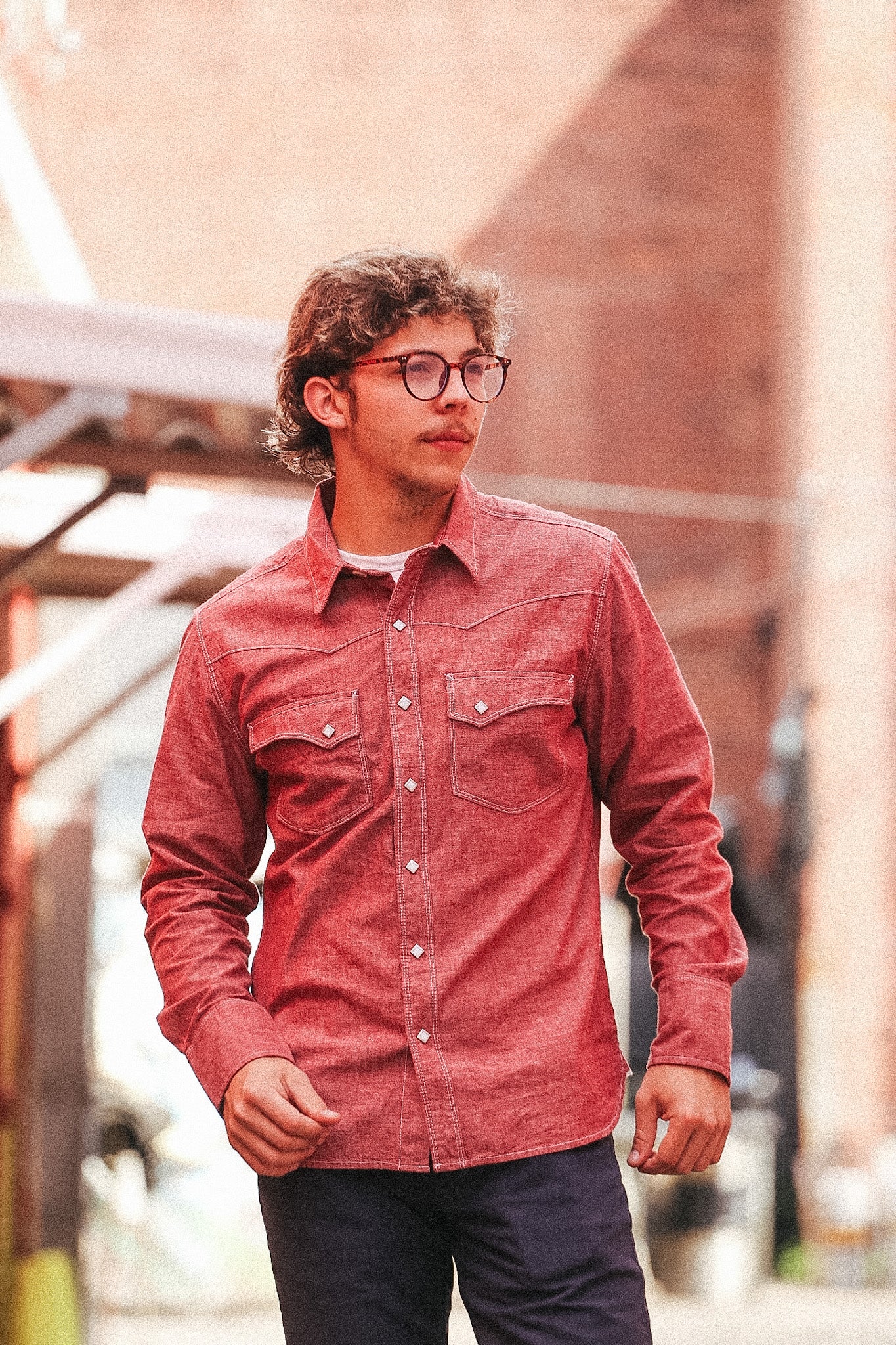 Man wearing a red shirt and glasses standing outdoors with blurred background