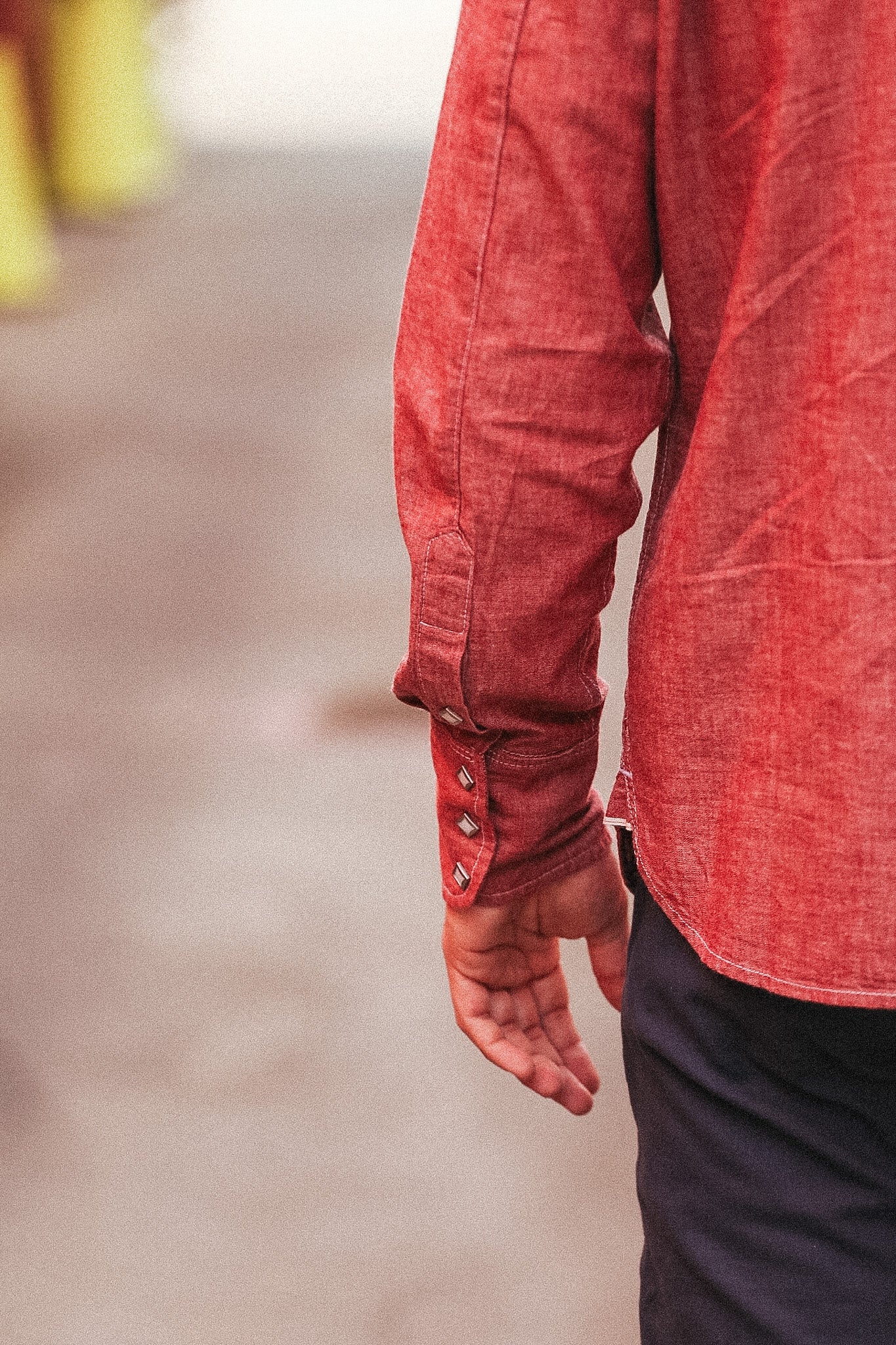 Close-up of a person wearing a red denim shirt with rolled-up sleeves on a blurred background.