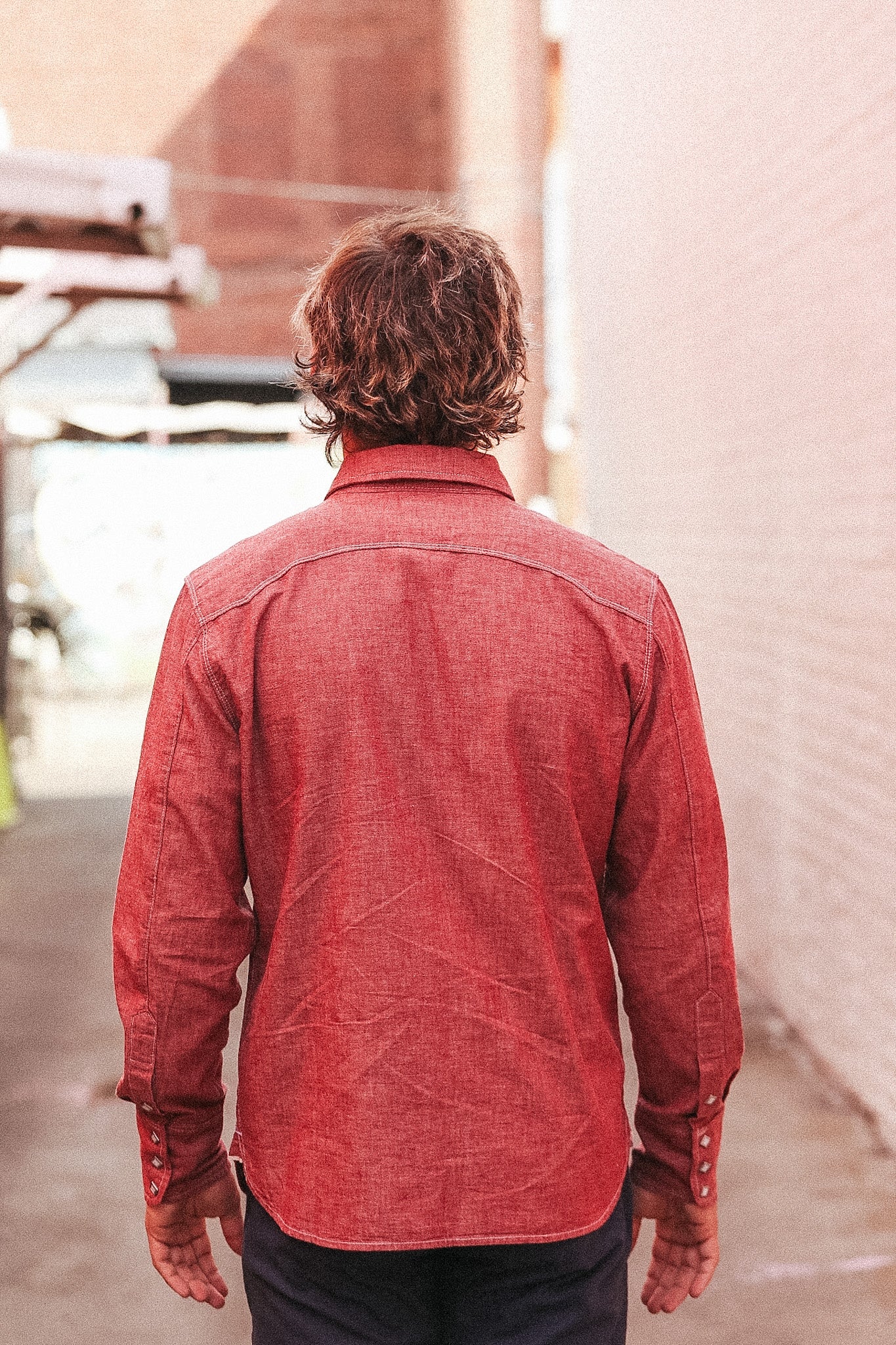 Person wearing a red denim shirt walking away from the camera with a blurred background