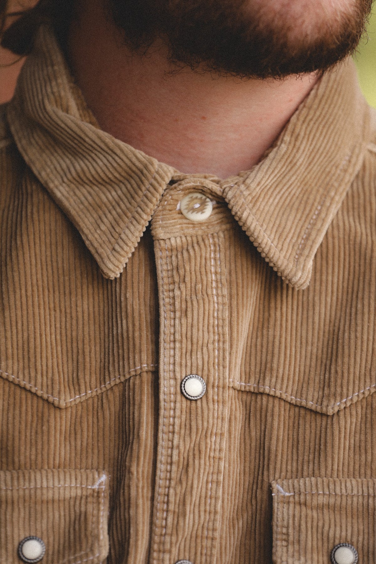 Close-up of a person wearing a tan corduroy button-up shirt with a pointed collar and silver-toned buttons.