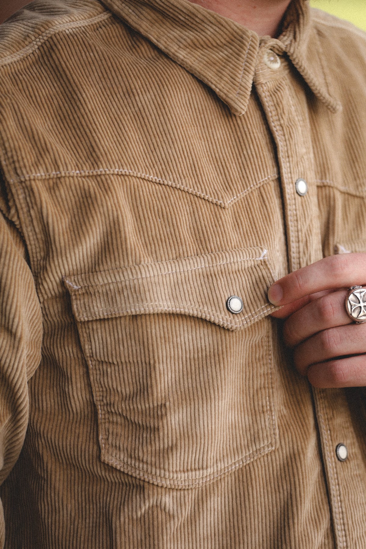Close-up of a person wearing a tan corduroy western-style button-up shirt with a chest pocket and silver snap buttons.