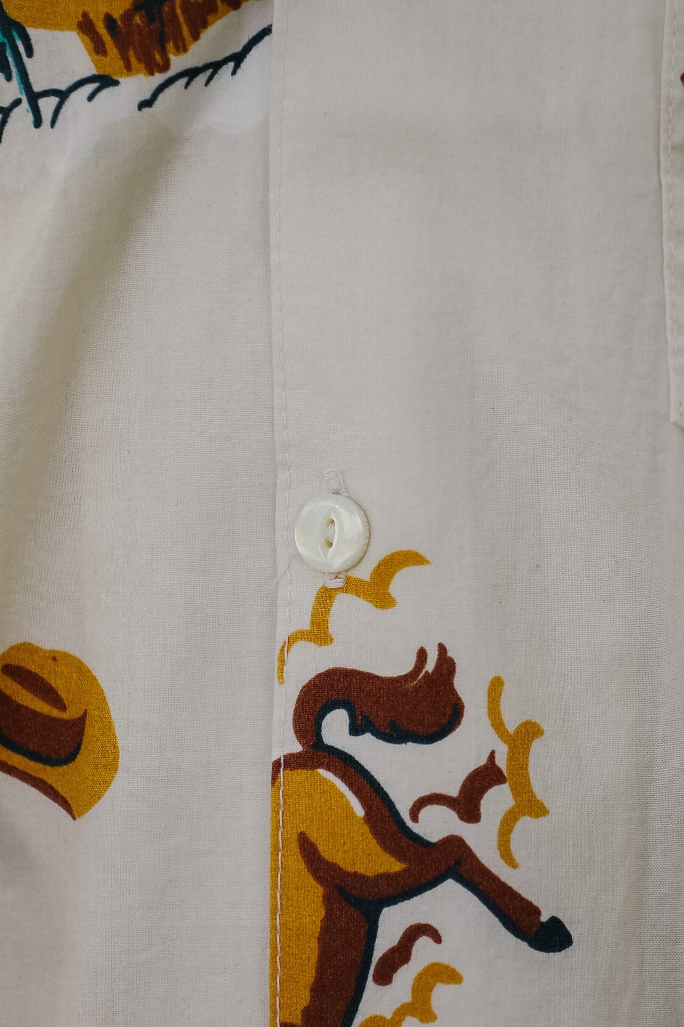 Close-up of a white button-up shirt featuring a colorful printed graphic of a cowboy riding a horse, with a yellow hat and dark blue decorative elements.