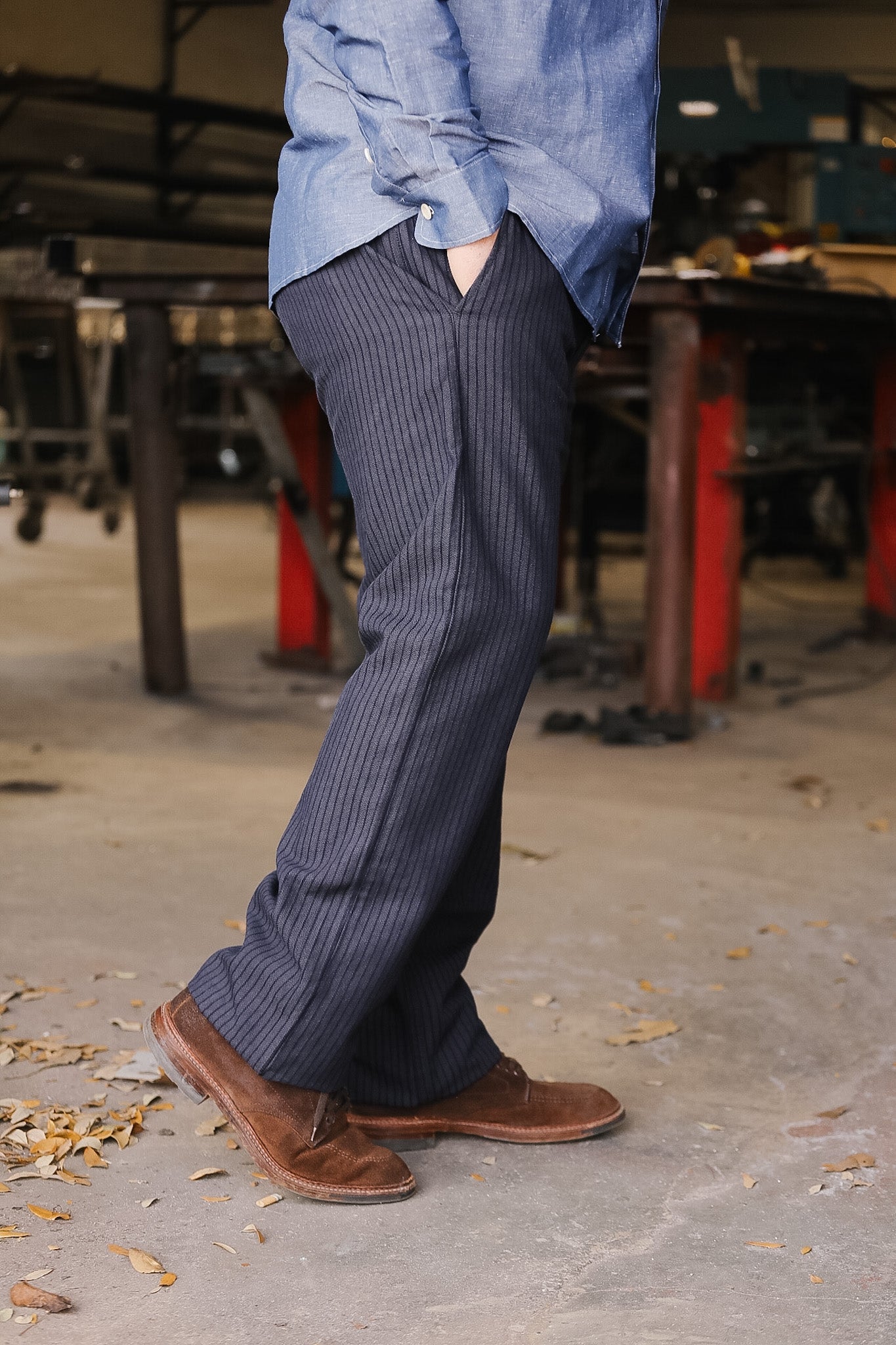 Person wearing blue shirt and striped pants with brown shoes in an industrial setting