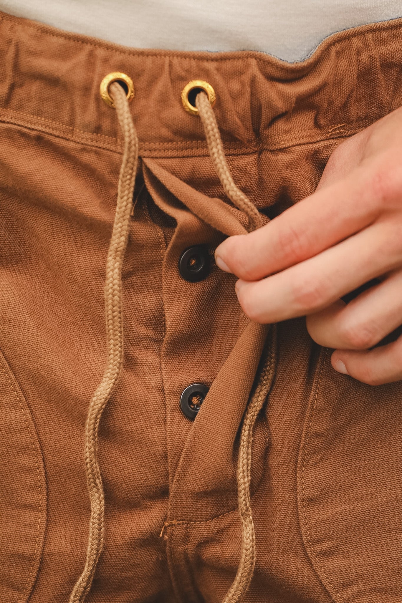 Close-up of brown pants with a hand adjusting the drawstring.