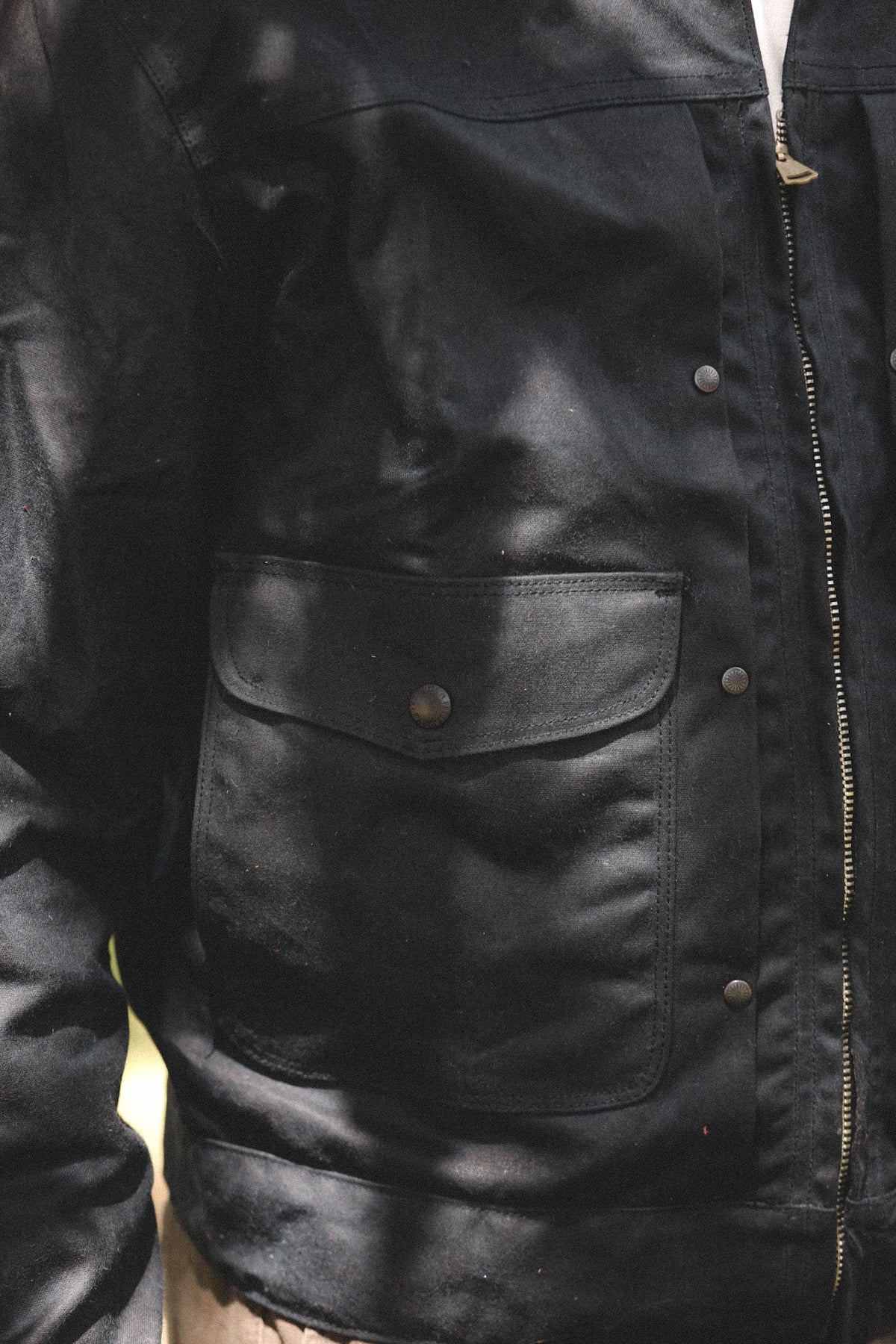 Close-up of a black leather jacket with a front flap pocket, metal snap button, and zipper detail.