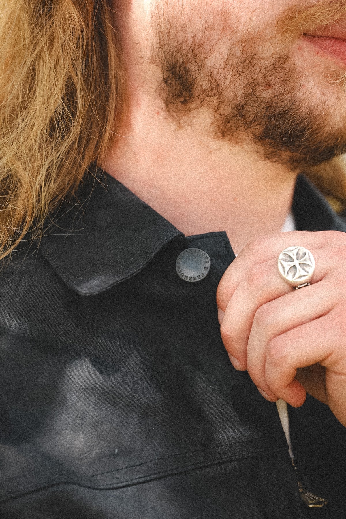 Close-up of a man wearing a large silver-toned ring with a starburst design on the finger, paired with a black leather jacket.
