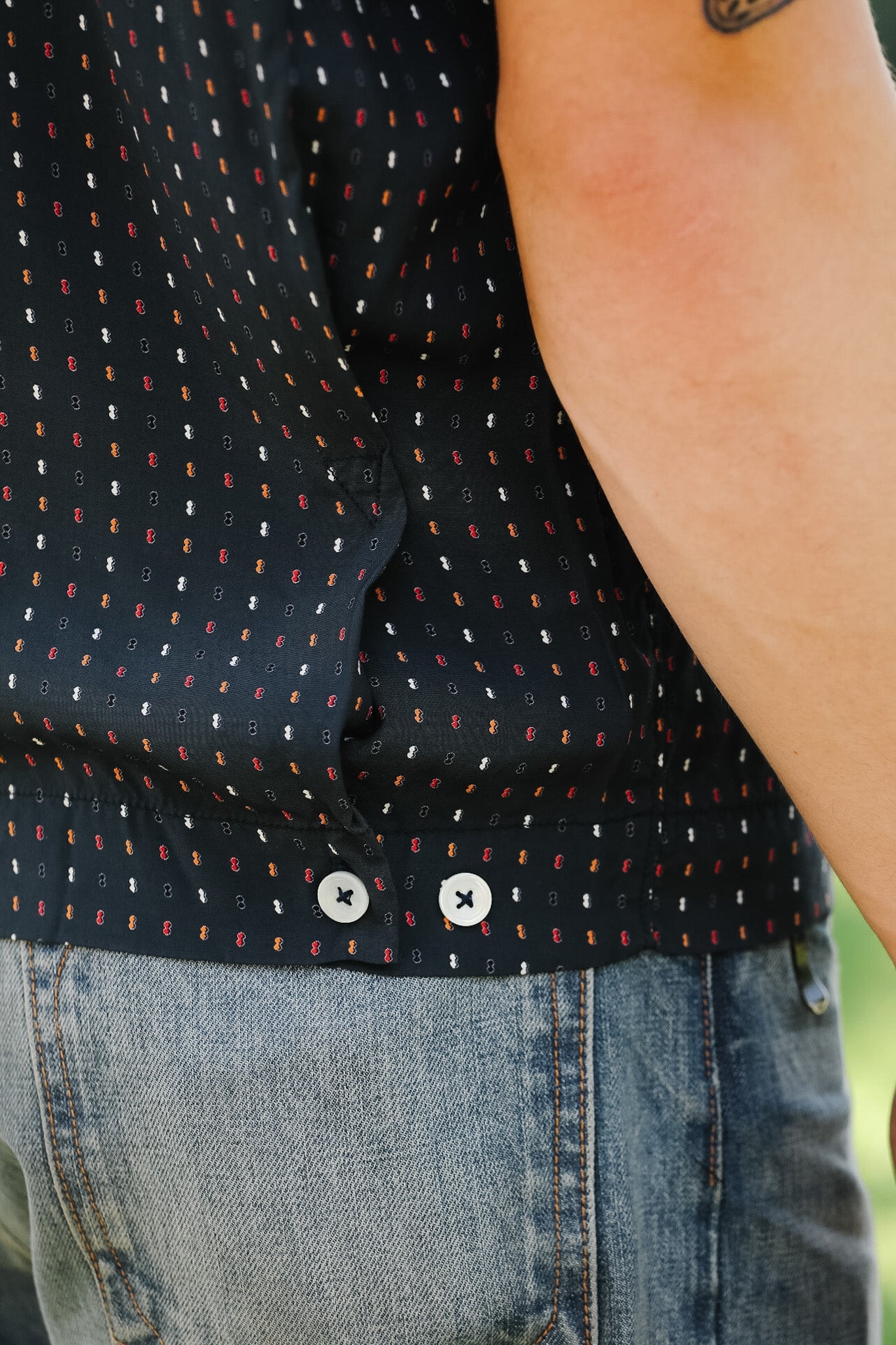 Close-up of a person wearing a black patterned shirt and blue jeans.