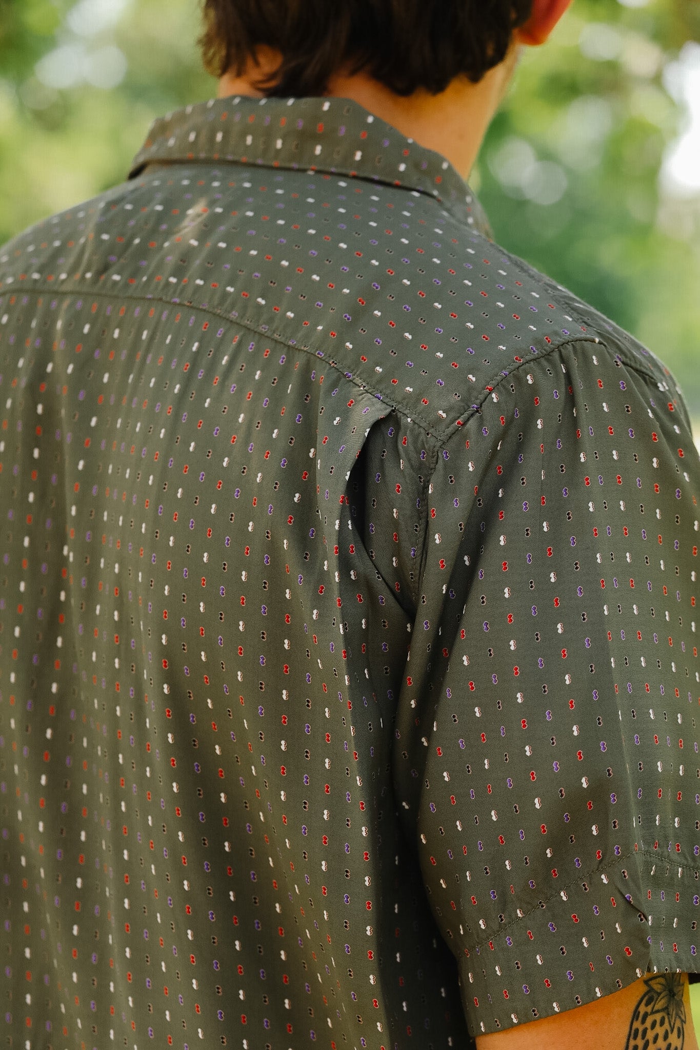 Person wearing a green patterned shirt with a blurred natural background