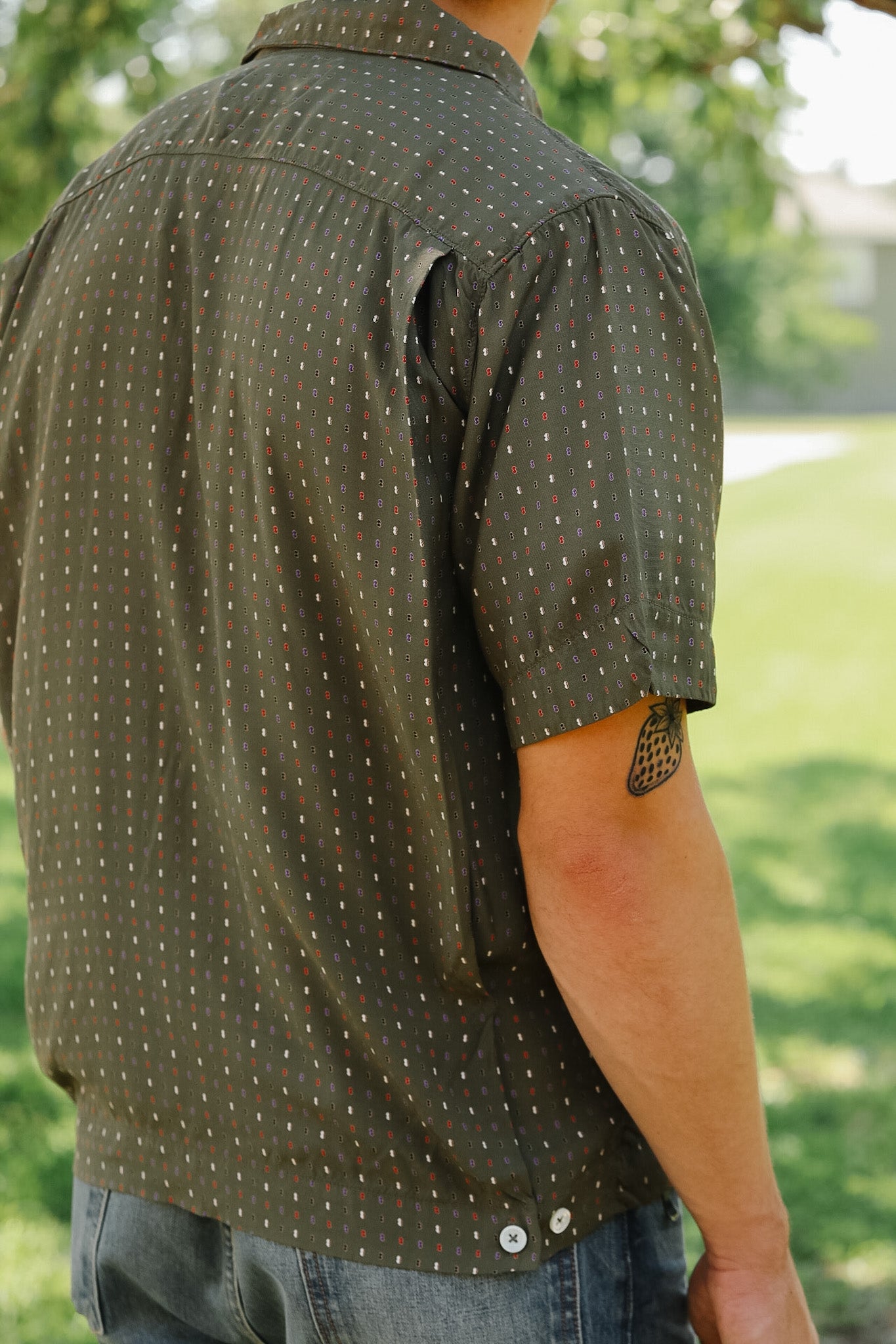 Person wearing a green patterned shirt with a blurred natural background
