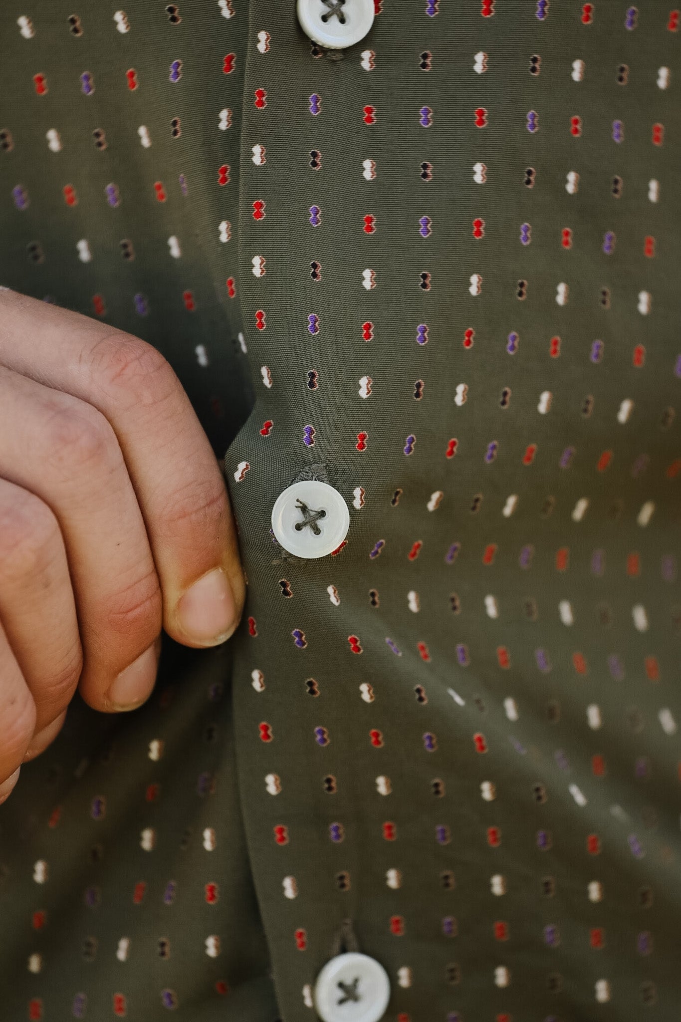 Close-up of a shirt with a pattern and buttons, held by a hand.