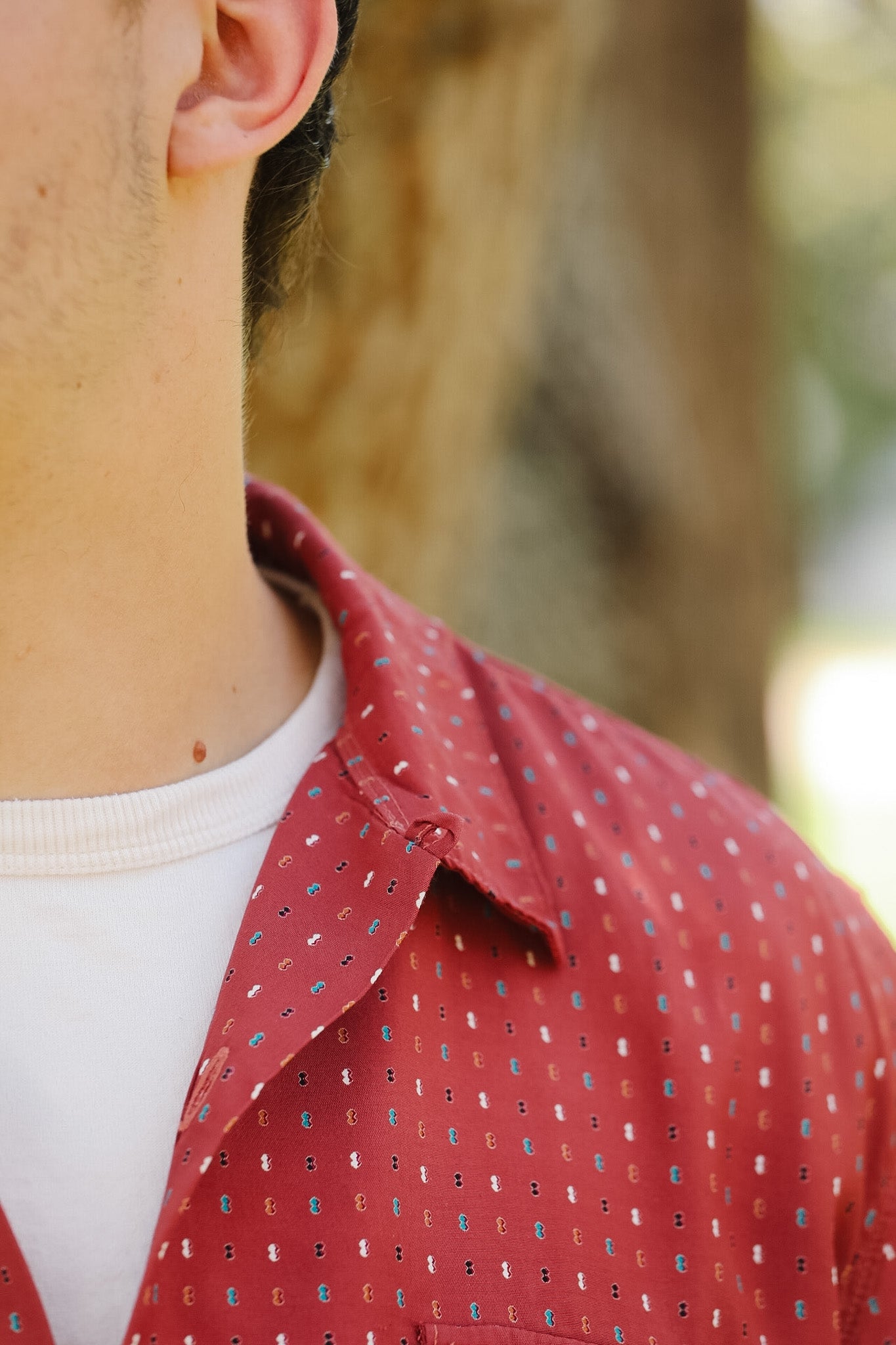 Close-up of a person wearing a red patterned shirt with a blurred natural background